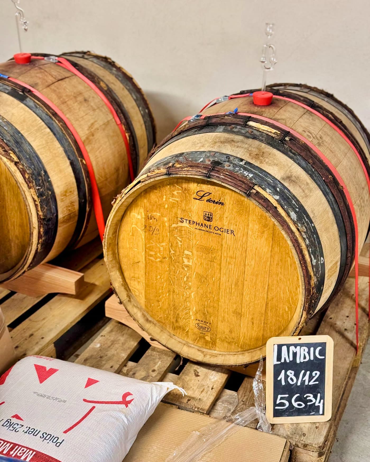 Fûts en bois empilés avec ardoise manuscrite 'LAMBIC' et sacs de malt au sol — Brasserie Georges