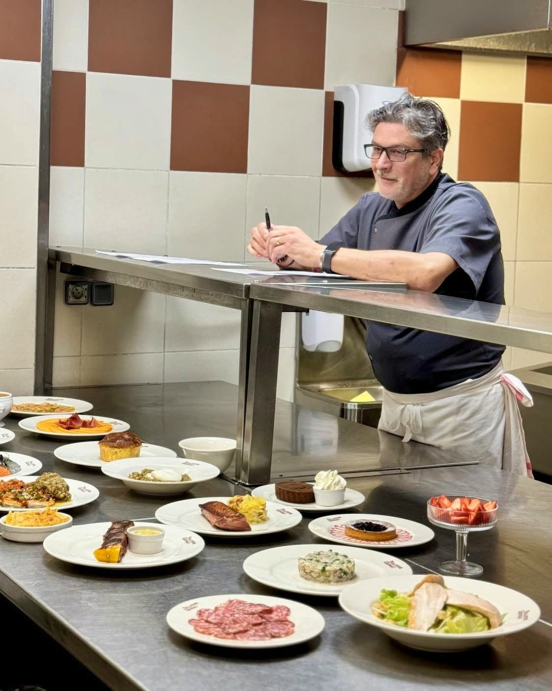 Chef en cuisine derrière un pass avec de nombreuses assiettes dressées, carnet en main — Brasserie Georges