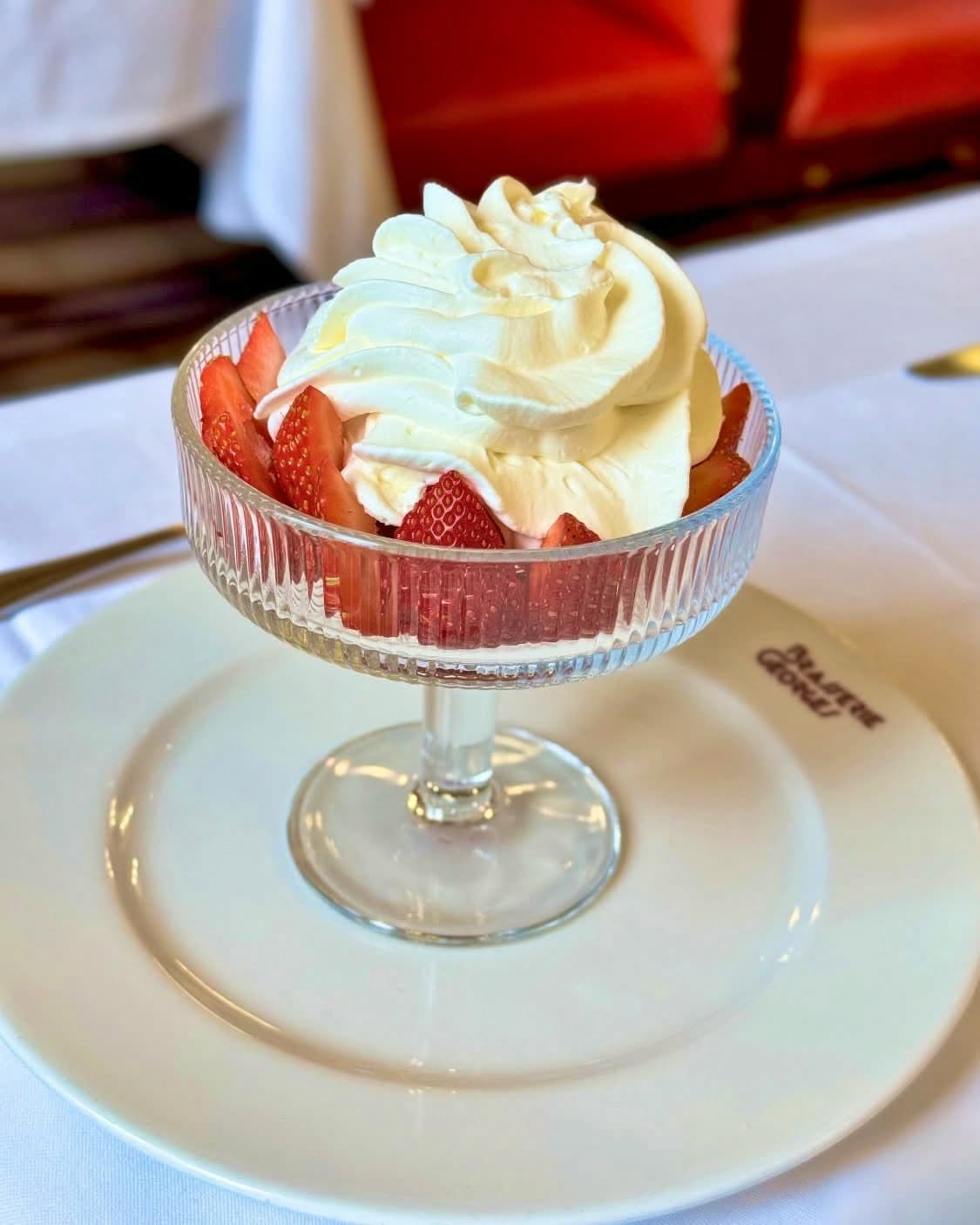 Coupe de fraises et chantilly sur assiette gravée Brasserie Georges, fond banquette rouge flou