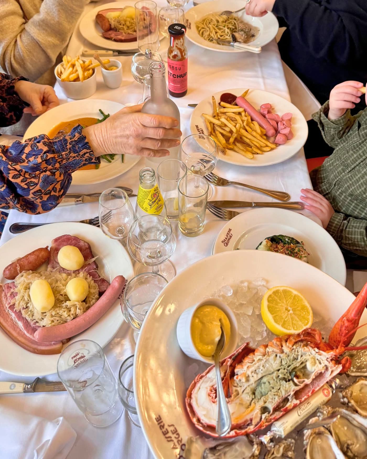 Vue de dessus d'une table généreuse : choucroute, frites, homard, boissons — Brasserie Georges