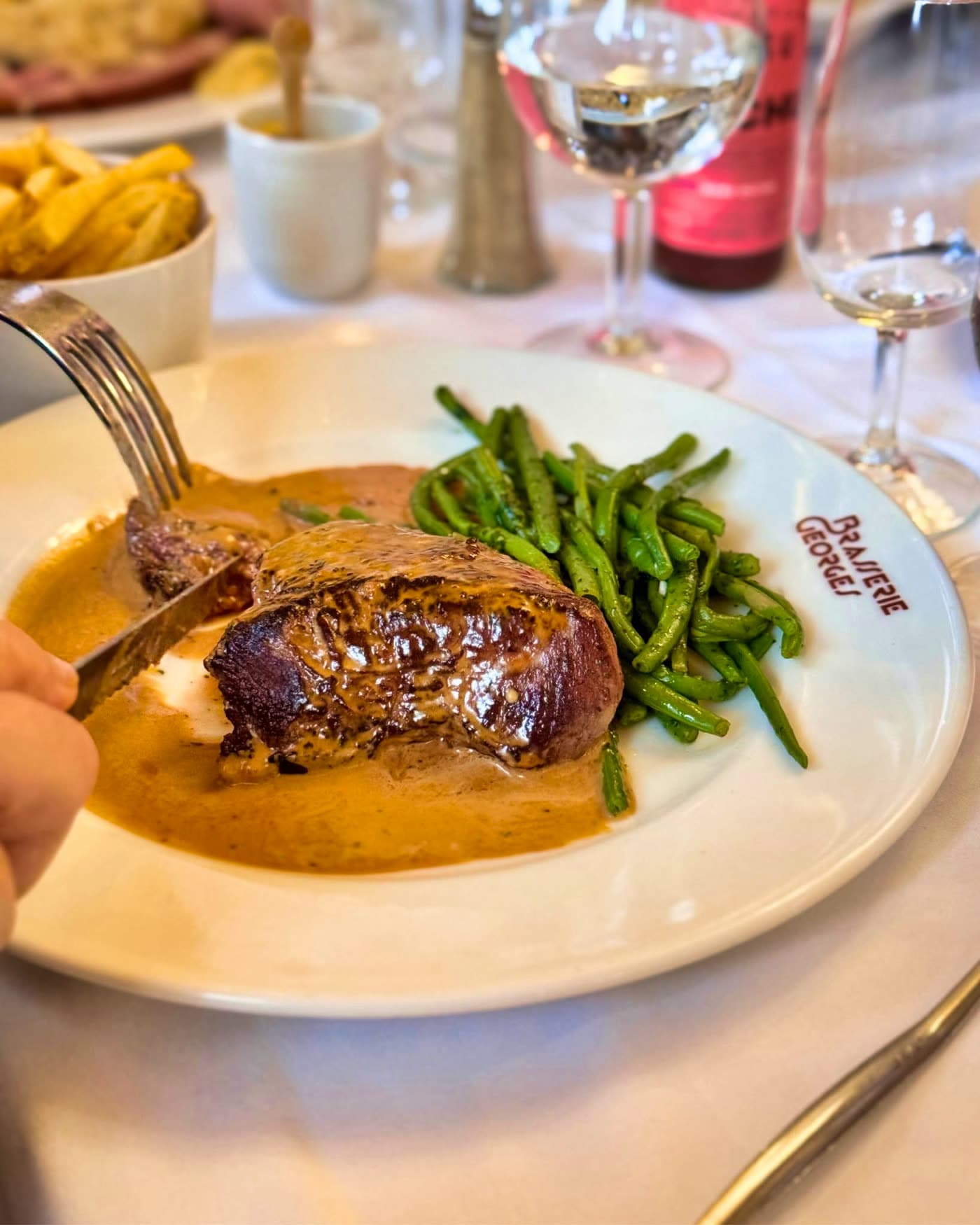Gros plan sur pièce de viande nappée de sauce et haricots verts, fourchette — Brasserie Georges
