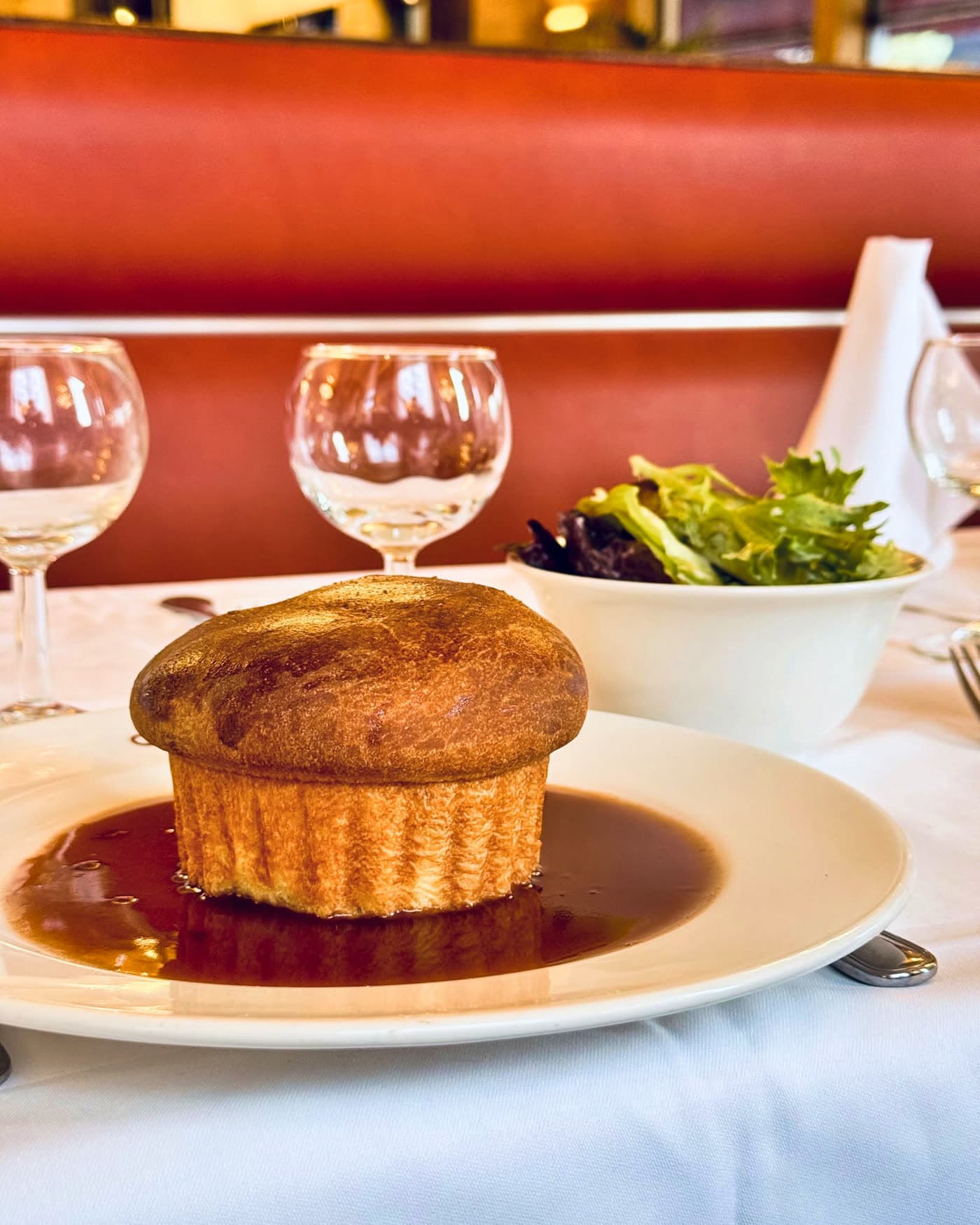 Soufflé doré sur assiette avec sauce et salade verte, verres à vin en fond — Brasserie Georges