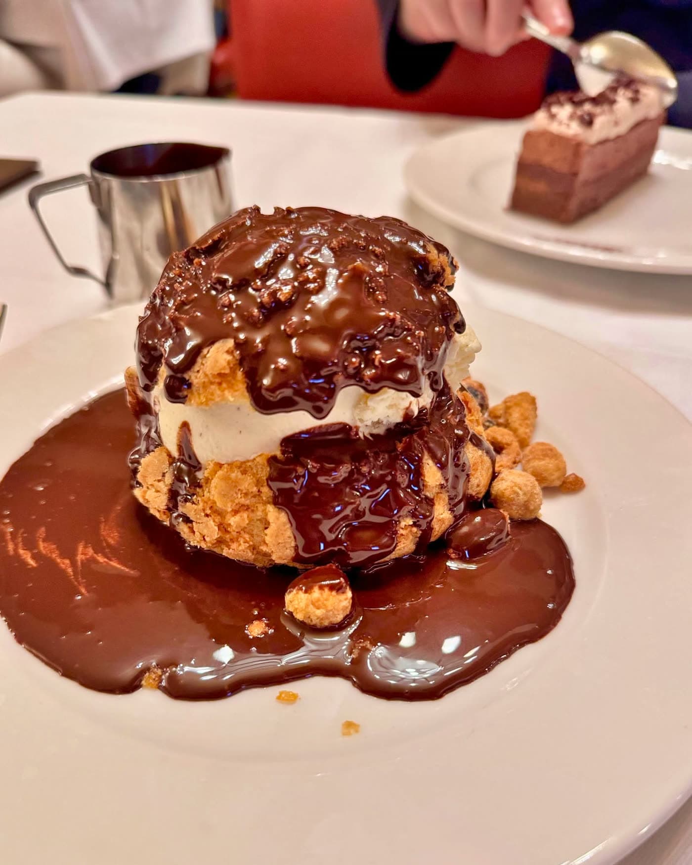 Profiterole glacée nappée de sauce chocolat sur assiette blanche, table dressée — Brasserie Georges