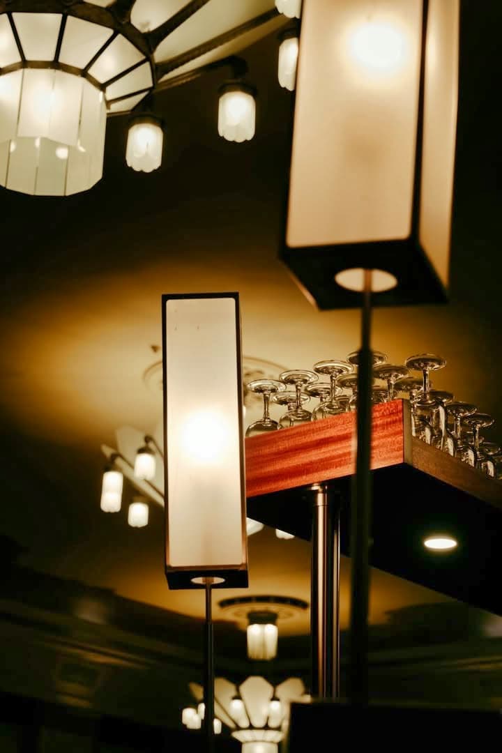 Appliques lumineuses et verres à pied rangés sur étagère bois, ambiance tamisée — Brasserie Georges