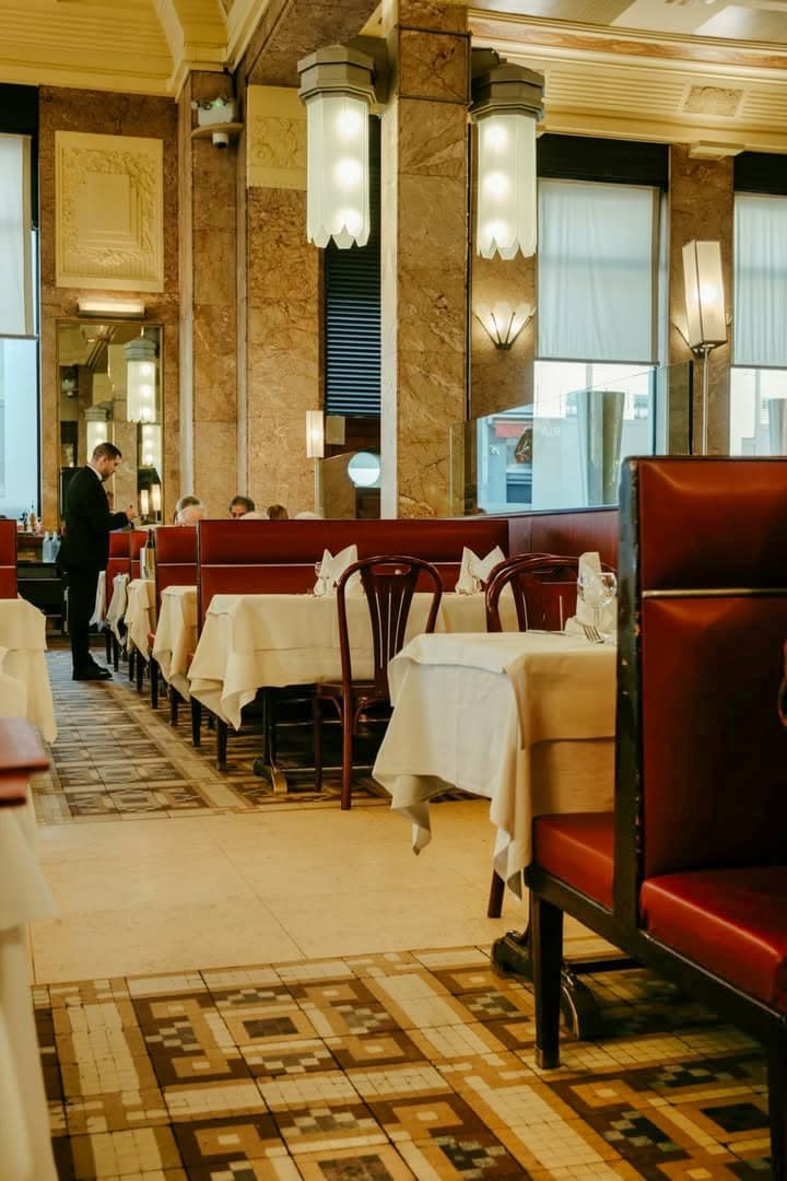 Grande salle Art déco vue en enfilade, colonnes marbre, banquettes rouges, serveur au fond — Brasserie Georges
