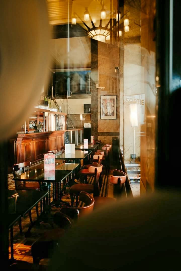 Comptoir du bar en bois vu à travers une vitre avec reflets, tabourets alignés — Brasserie Georges
