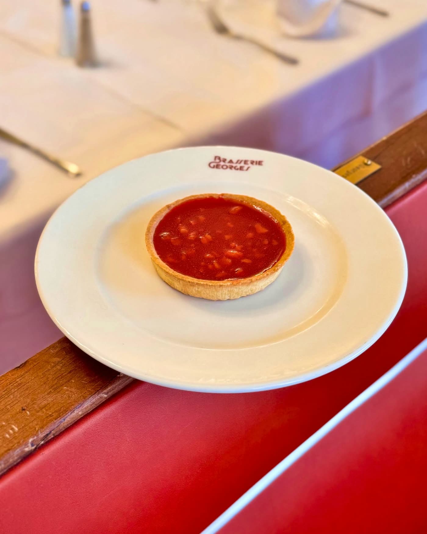 Tartelette aux fruits rouges sur assiette blanche logotée posée sur banquette rouge — Brasserie Georges