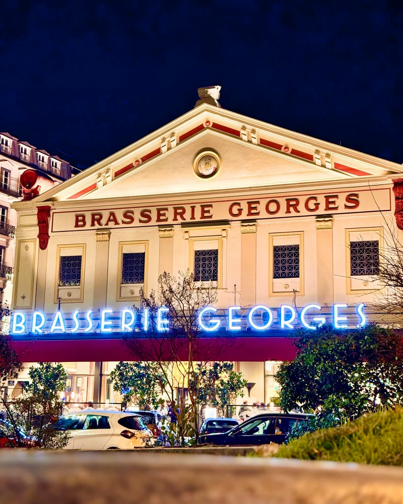 Façade illuminée la nuit avec enseigne néon Brasserie Georges, ciel bleu nuit