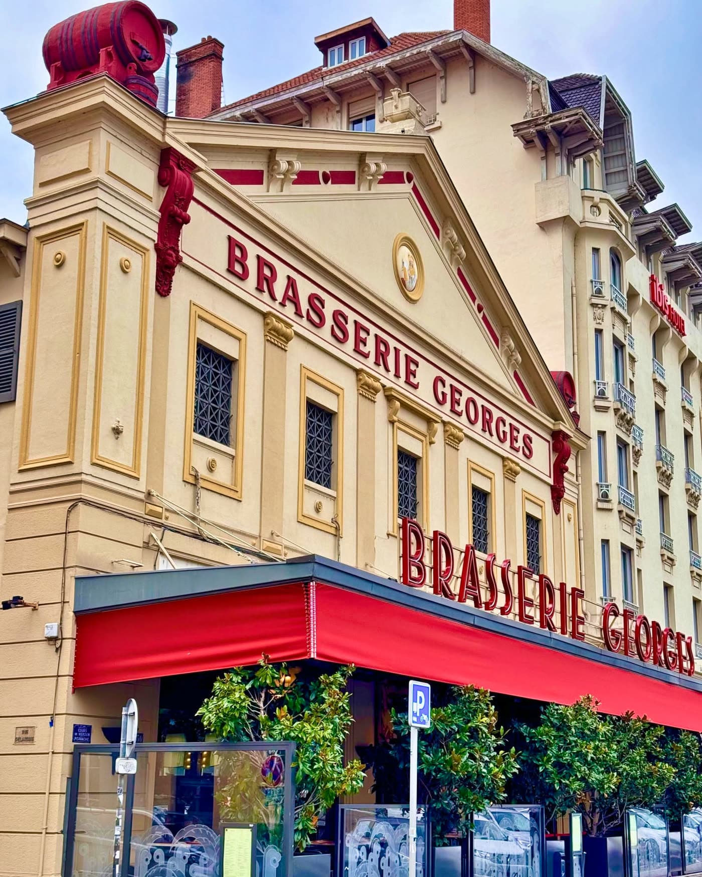 Façade complète de la Brasserie Georges de jour avec enseigne et auvent rouge
