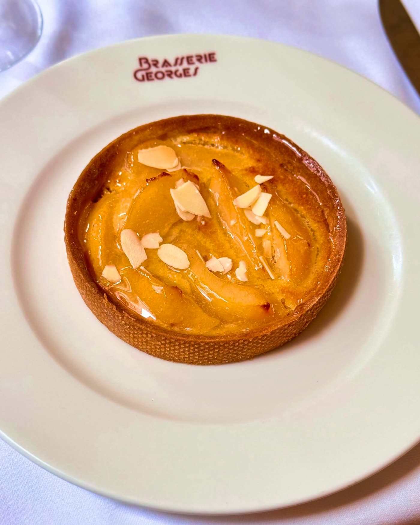 Tarte amandine garnie d'amandes effilées sur assiette blanche — Brasserie Georges