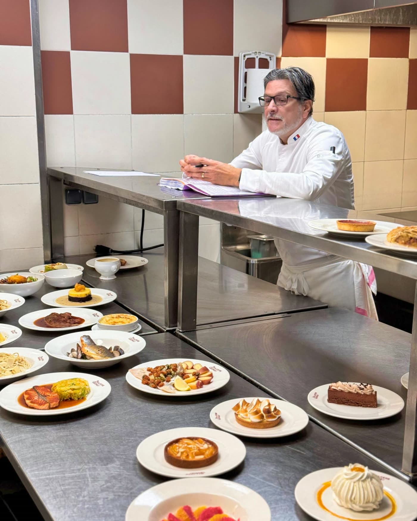 Chef en cuisine devant une longue rangée d'assiettes de desserts dressées — Brasserie Georges