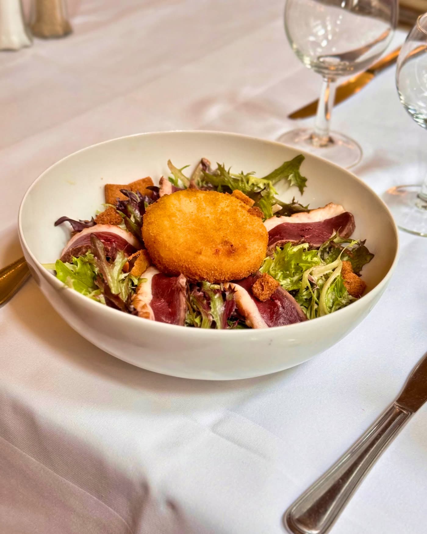 Salade composée avec foie gras pané et magret sur mesclun, verres à pied en fond — Brasserie Georges