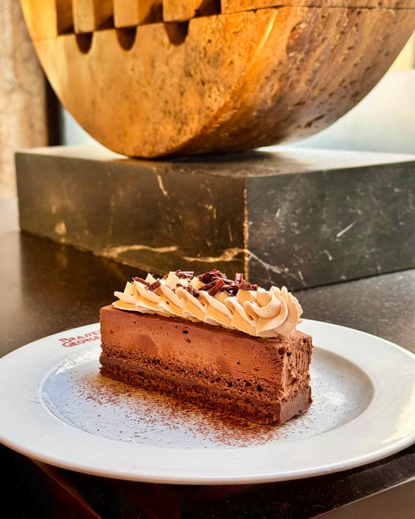 Part de gâteau au chocolat et chantilly sur socle en bois sculpté sombre — Brasserie Georges