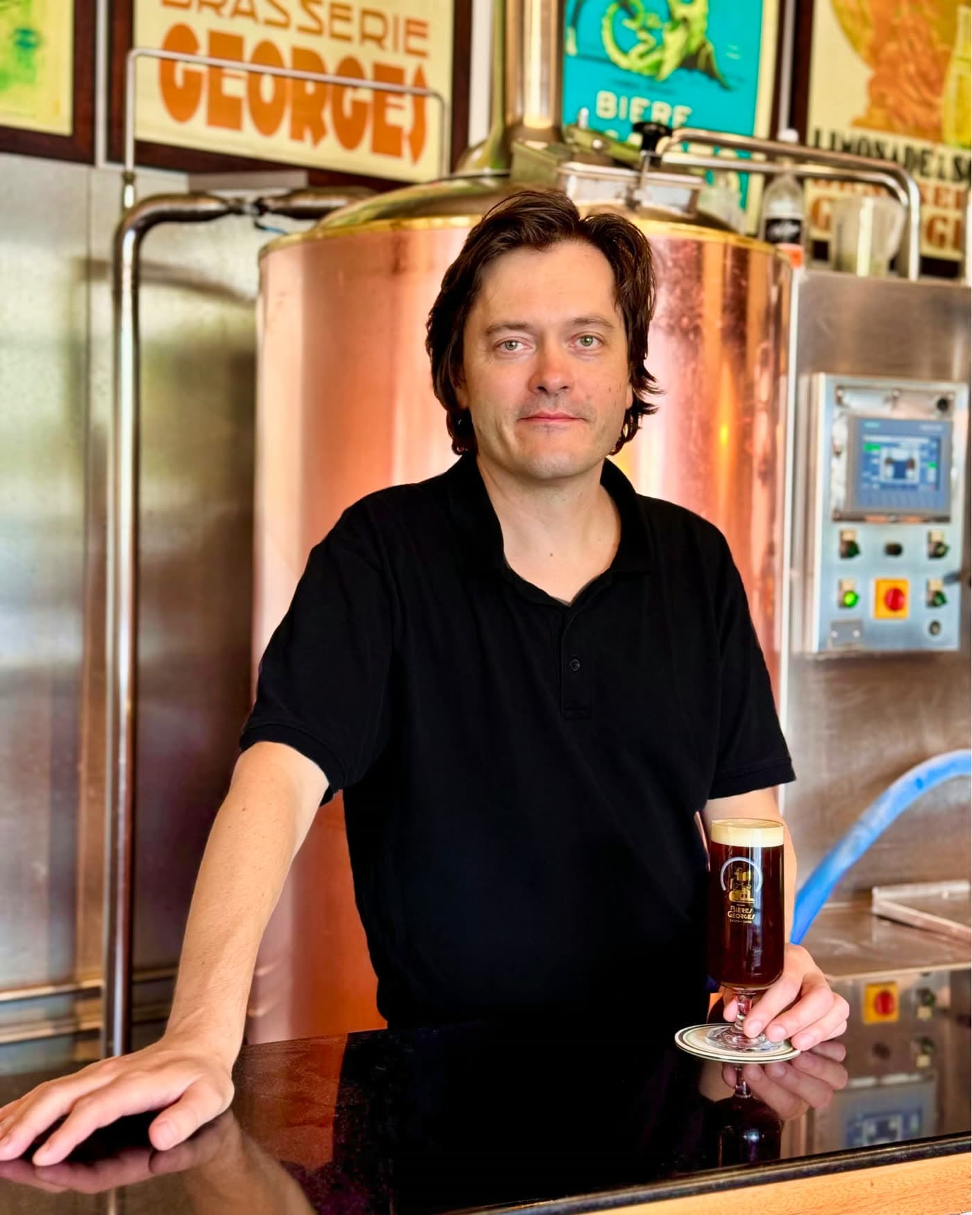 Portrait d'un brasseur tenant un verre de bière ambrée devant une cuve en cuivre — Brasserie Georges