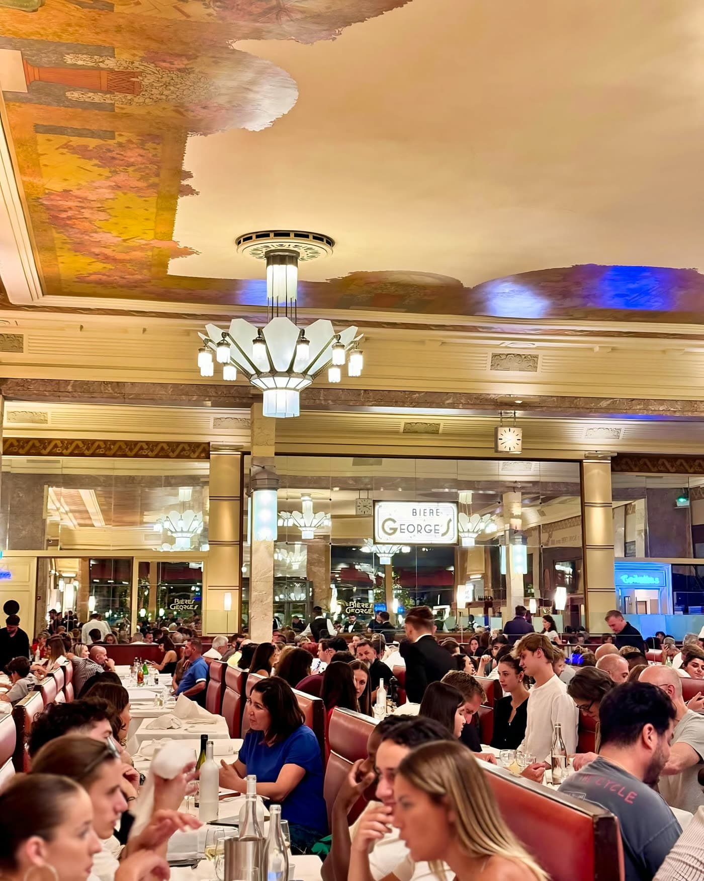 Vue d'ensemble de la salle bondée avec plafond peint et lustres Art déco — Brasserie Georges