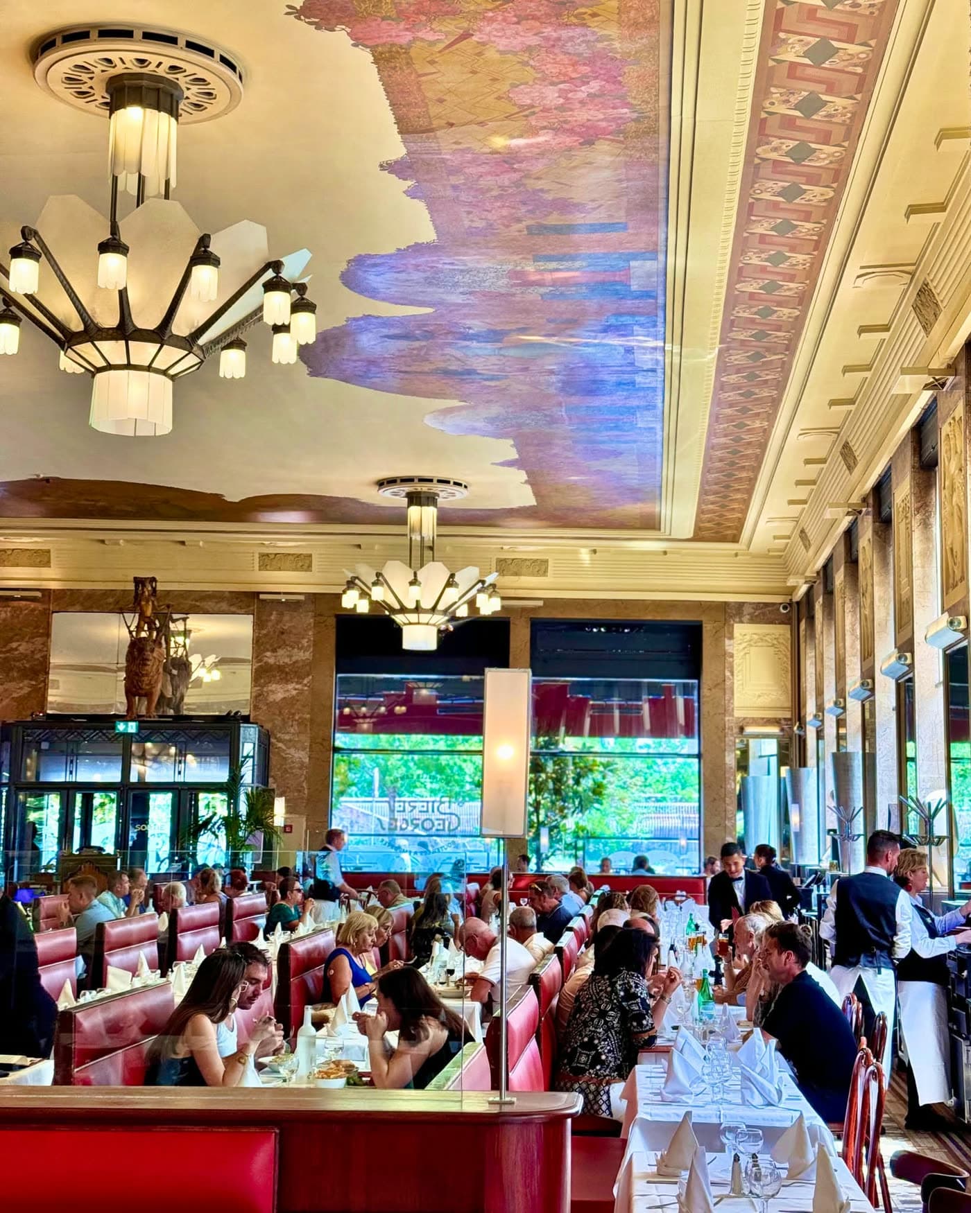 Grande salle animée en soirée avec plafond peint marbré, lustres et clients en tenue — Brasserie Georges