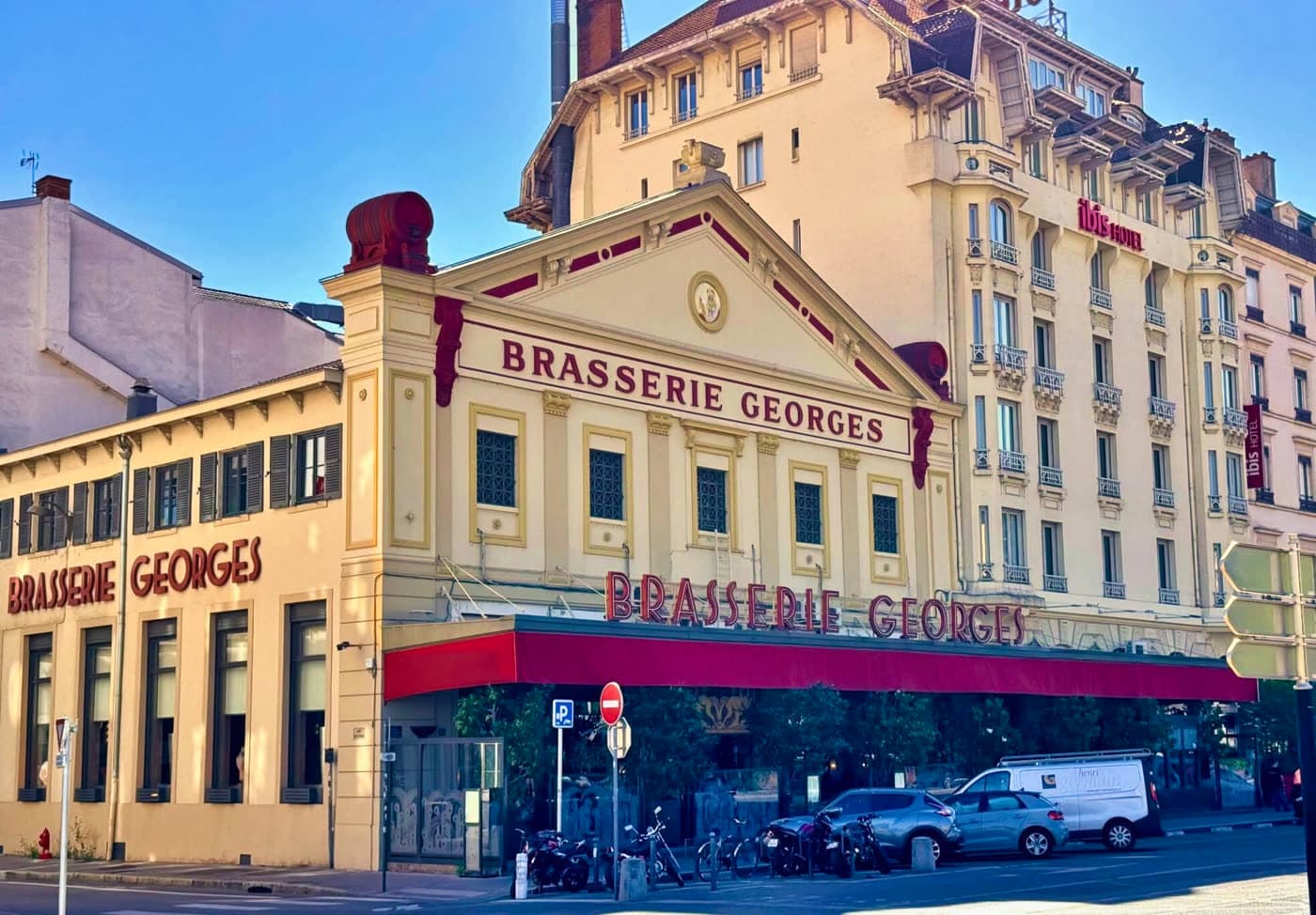 Façade d'angle Brasserie Georges avec double enseigne, auvent rouge et rue animée