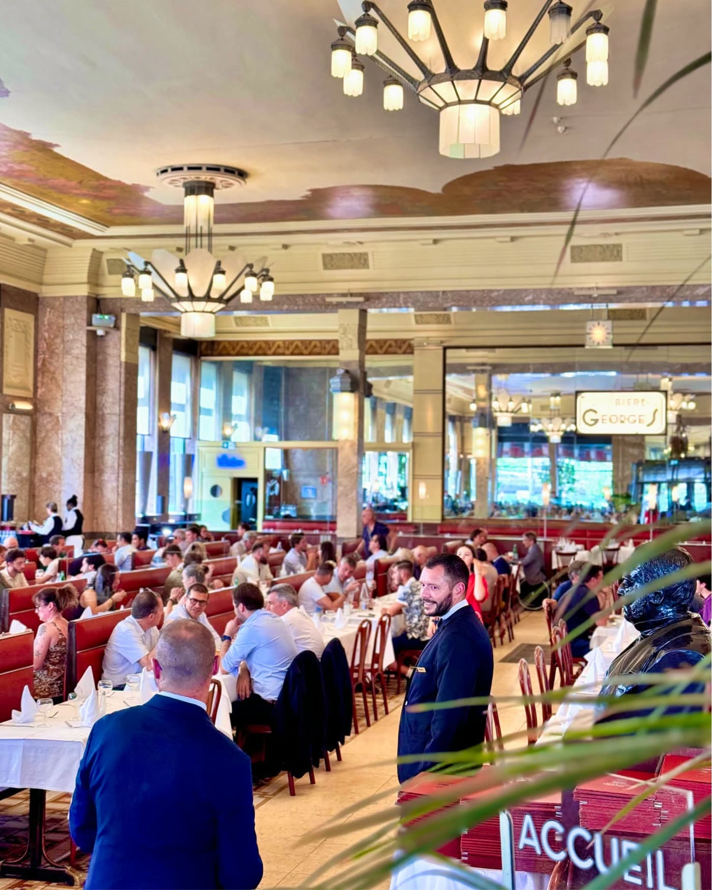 Vue de la salle avec zone d'accueil, maître d'hôtel debout et clients attablés — Brasserie Georges