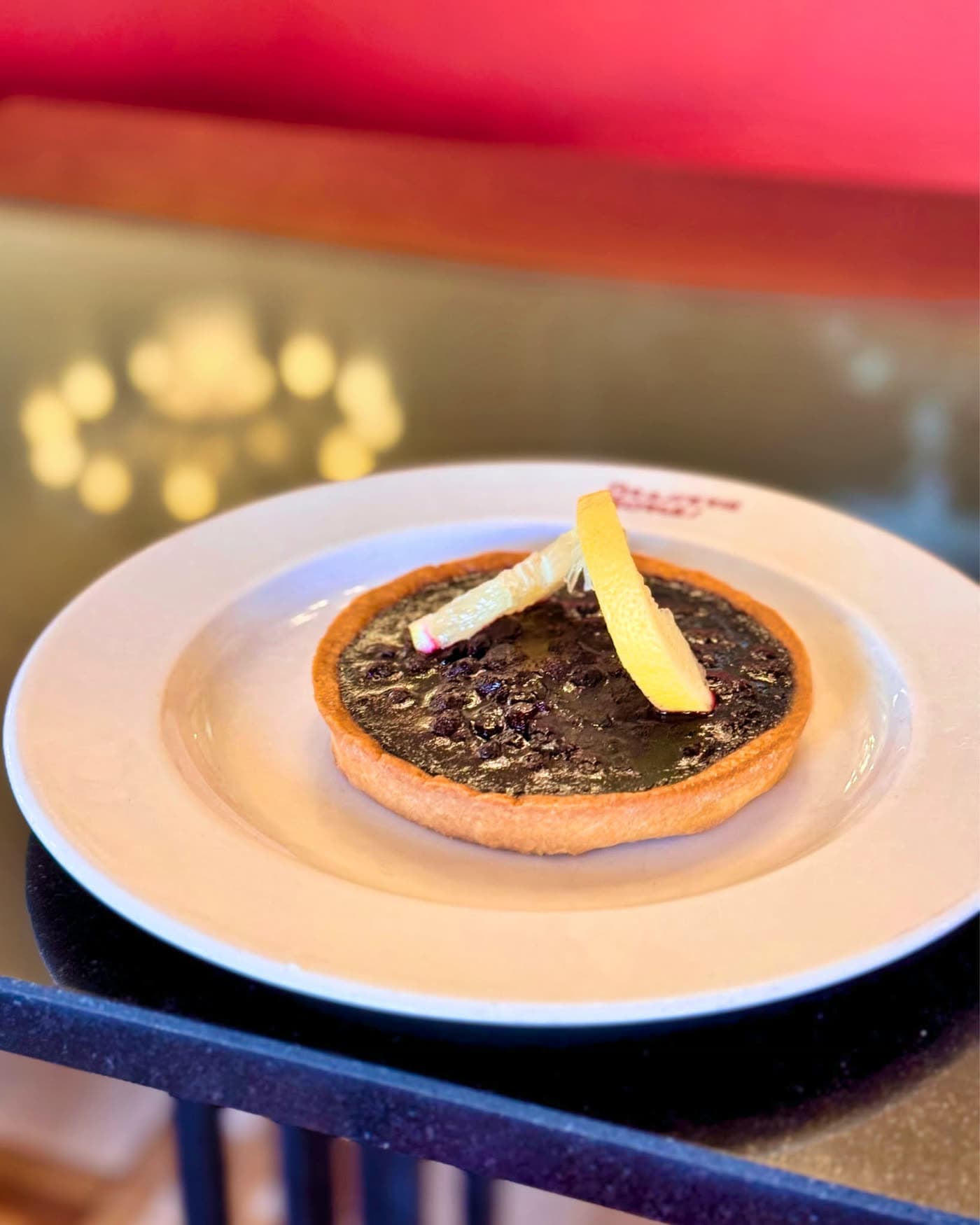 Part de tarte chocolatée nappée avec zestes de citron sur assiette blanche, fond rouge flou — Brasserie Georges