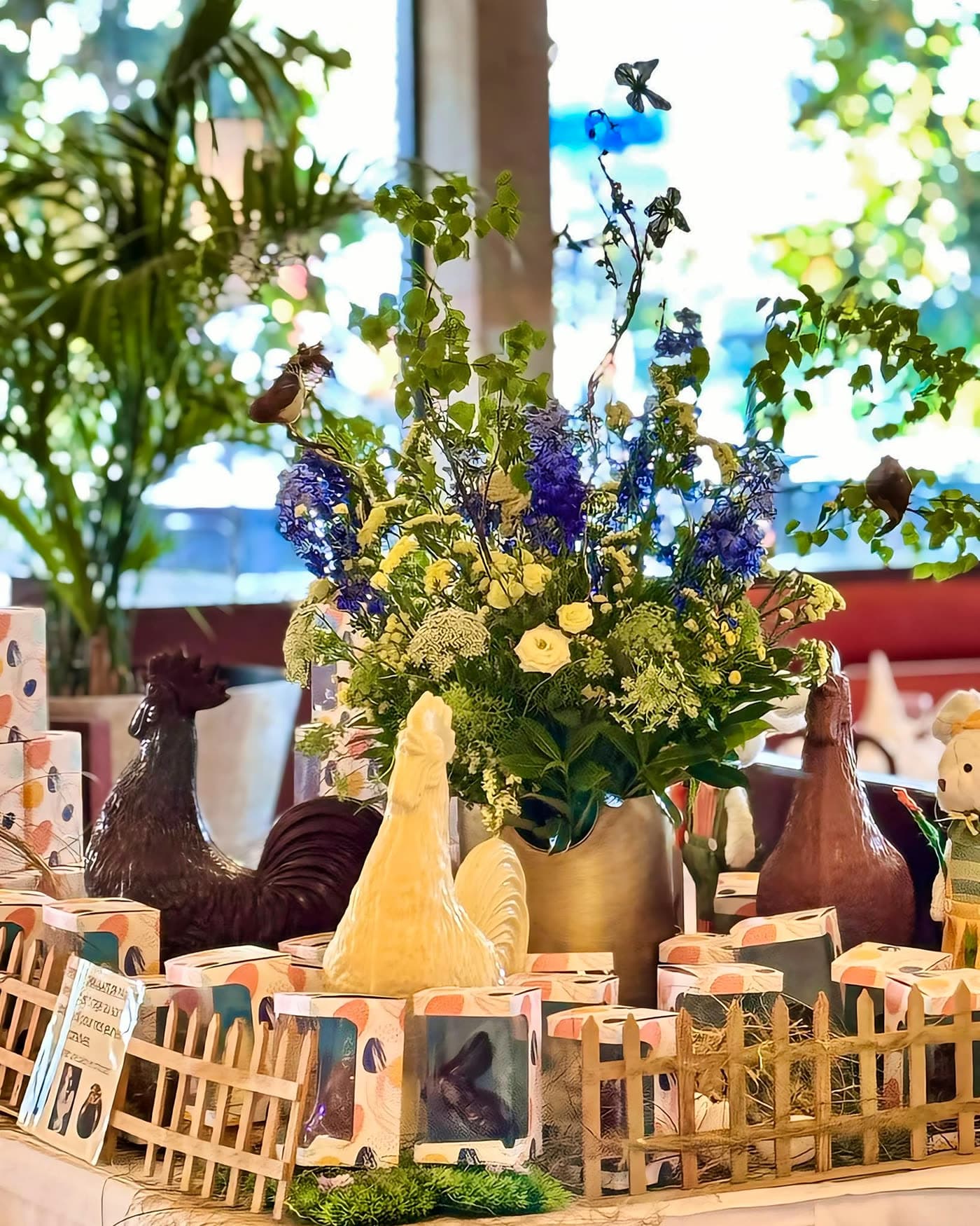 Composition de Pâques avec coqs en chocolat et bouquet près d'une vitrine végétalisée — Brasserie Georges