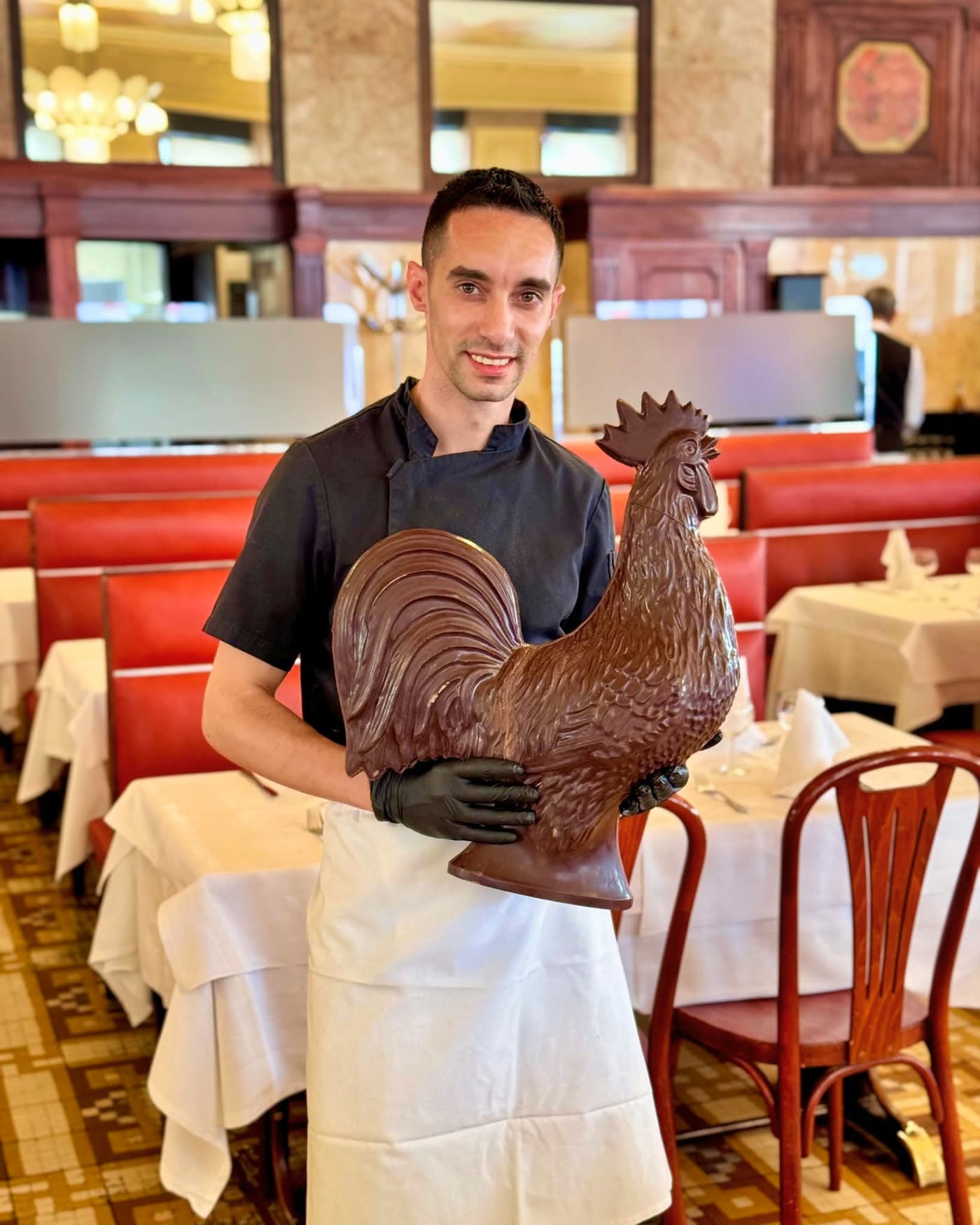 Cuisinier en tablier tenant un grand coq en chocolat dans la salle — Brasserie Georges