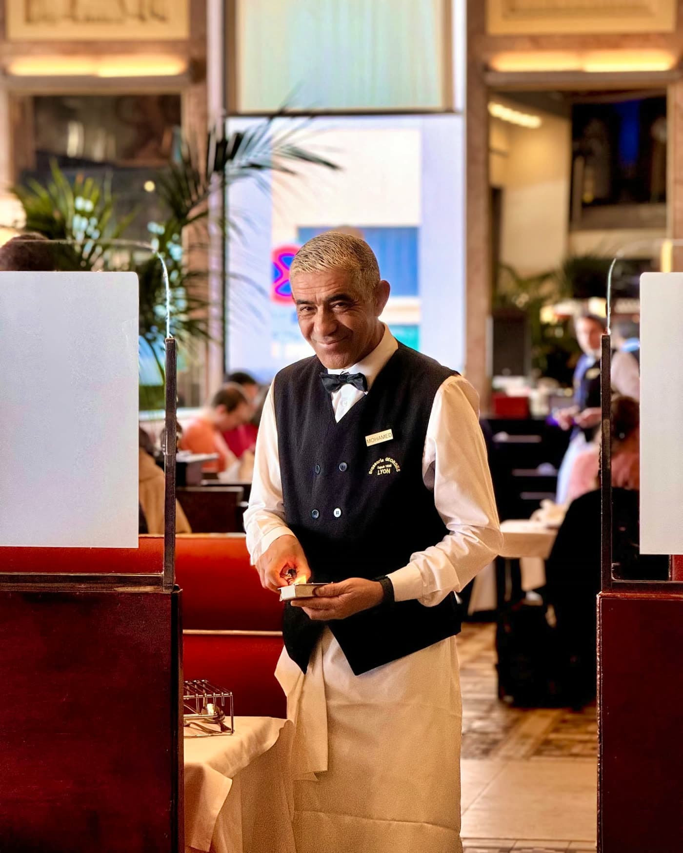 Serveur en gilet et nœud papillon souriant dans l'entrée de la salle — Brasserie Georges