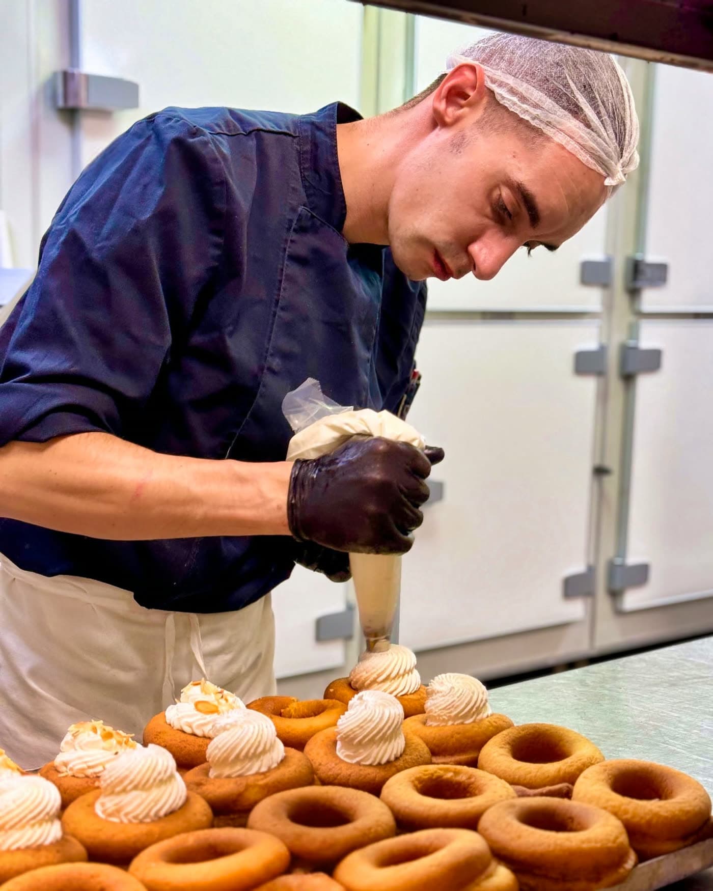 Pâtissier garnissant de chantilly des choux/religieuses en cuisine — Brasserie Georges