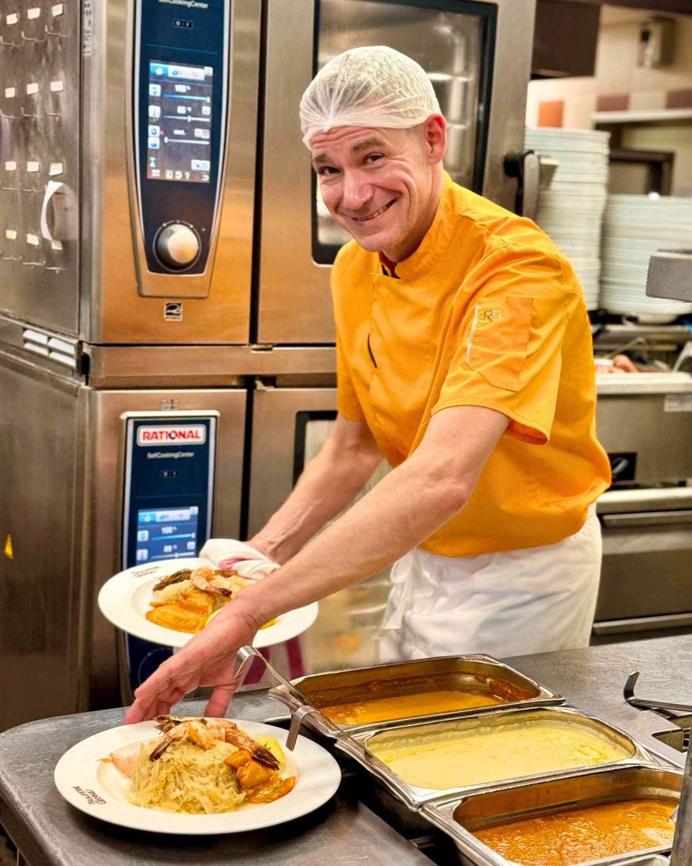 Cuisinier souriant dressant deux assiettes de choucroute devant un four professionnel — Brasserie Georges