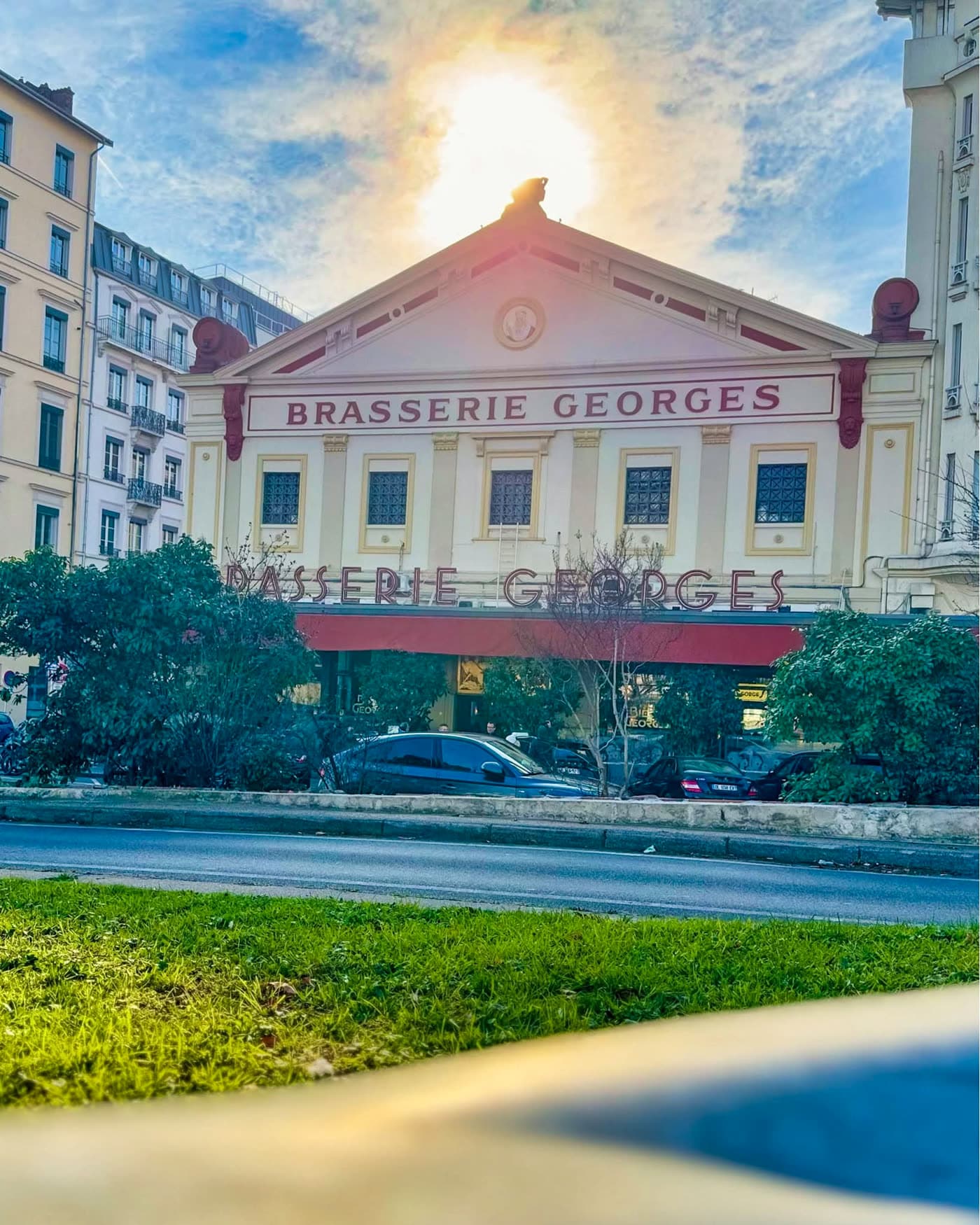 Façade de la Brasserie Georges avec enseigne, soleil et ciel bleu en contre-jour