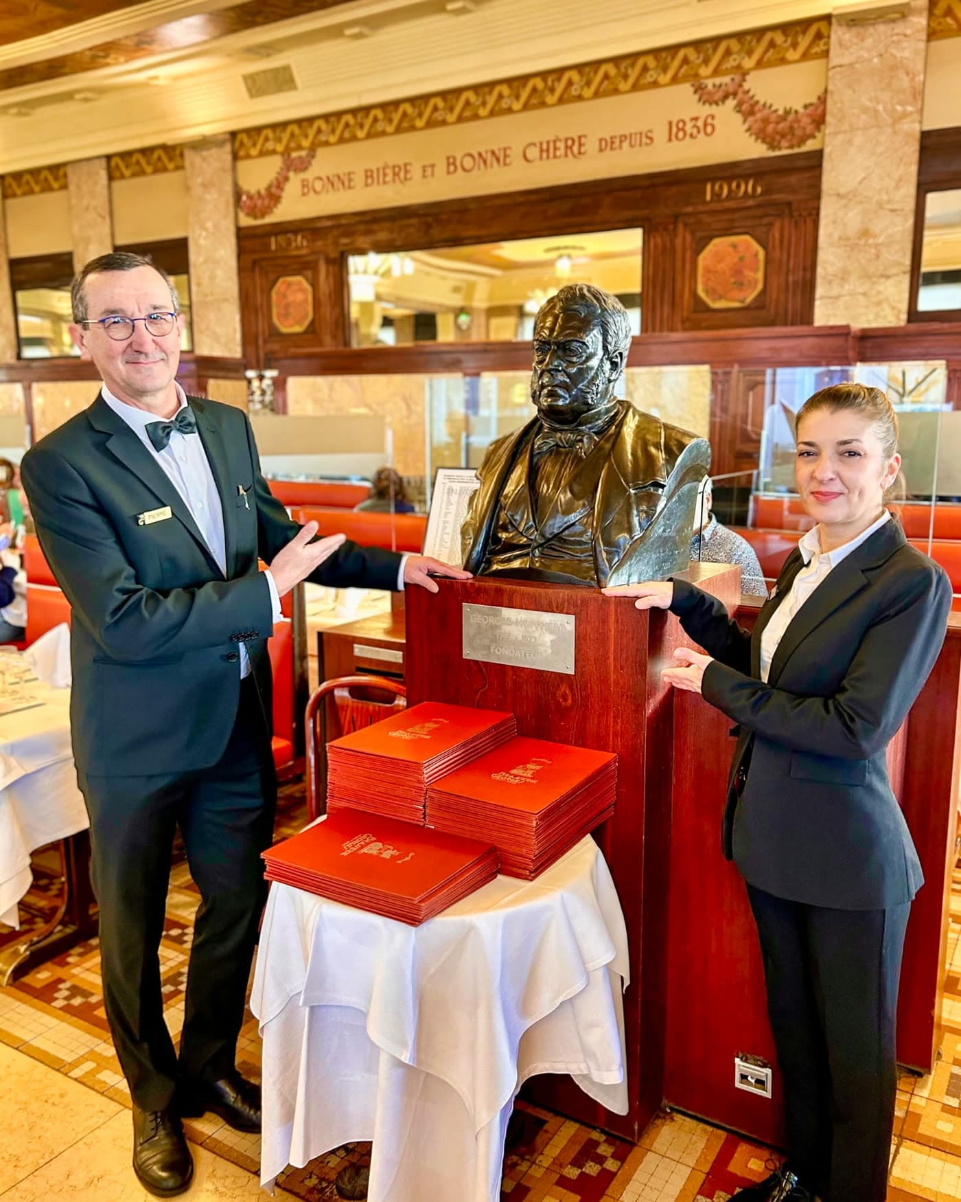 Maître d'hôtel et hôtesse posant en costume près du buste avec cartes de menu — Brasserie Georges