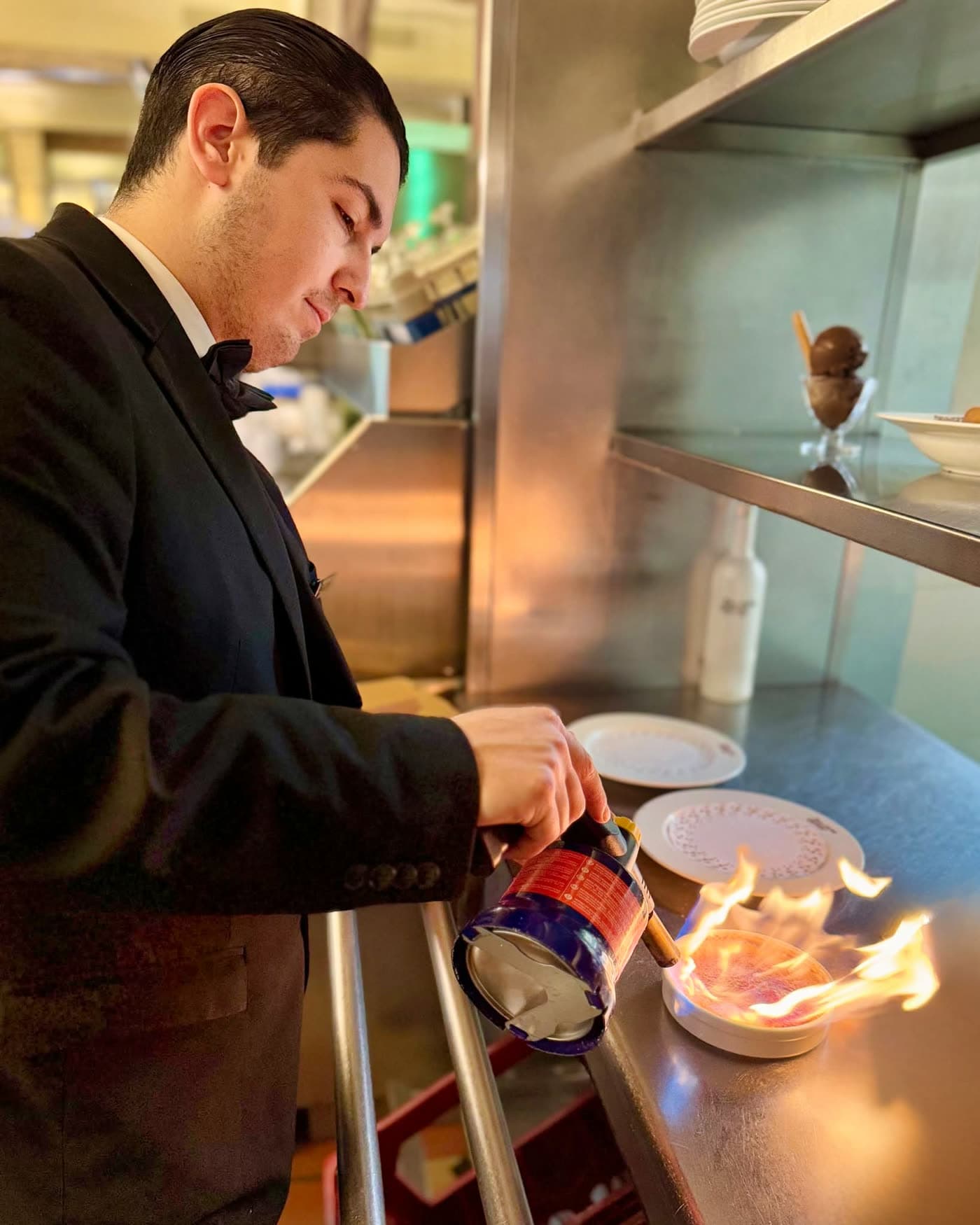 Serveur en smoking flambant un dessert au comptoir de cuisine, flamme visible — Brasserie Georges
