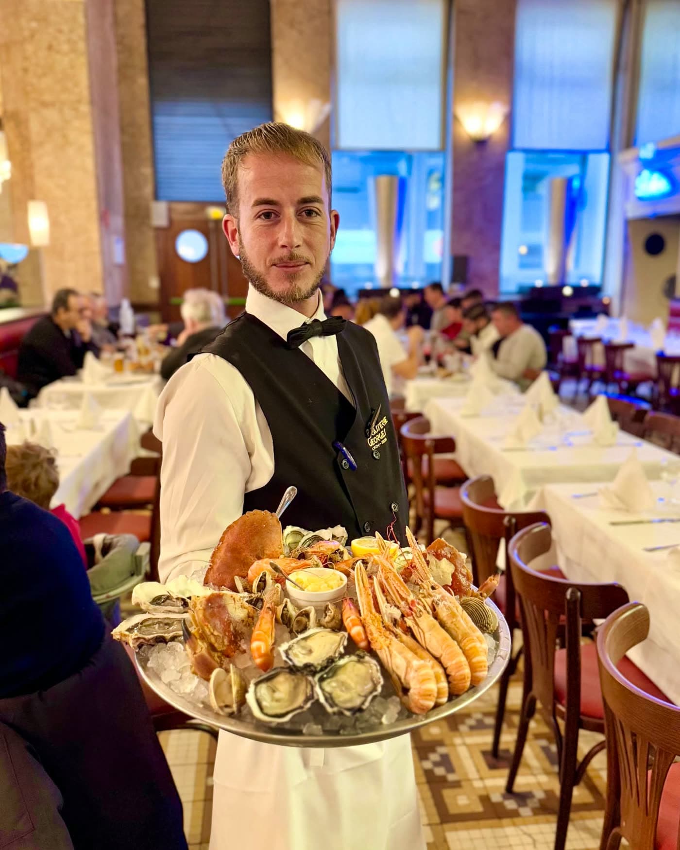 Serveur tenant un grand plateau de fruits de mer glacé dans la salle — Brasserie Georges