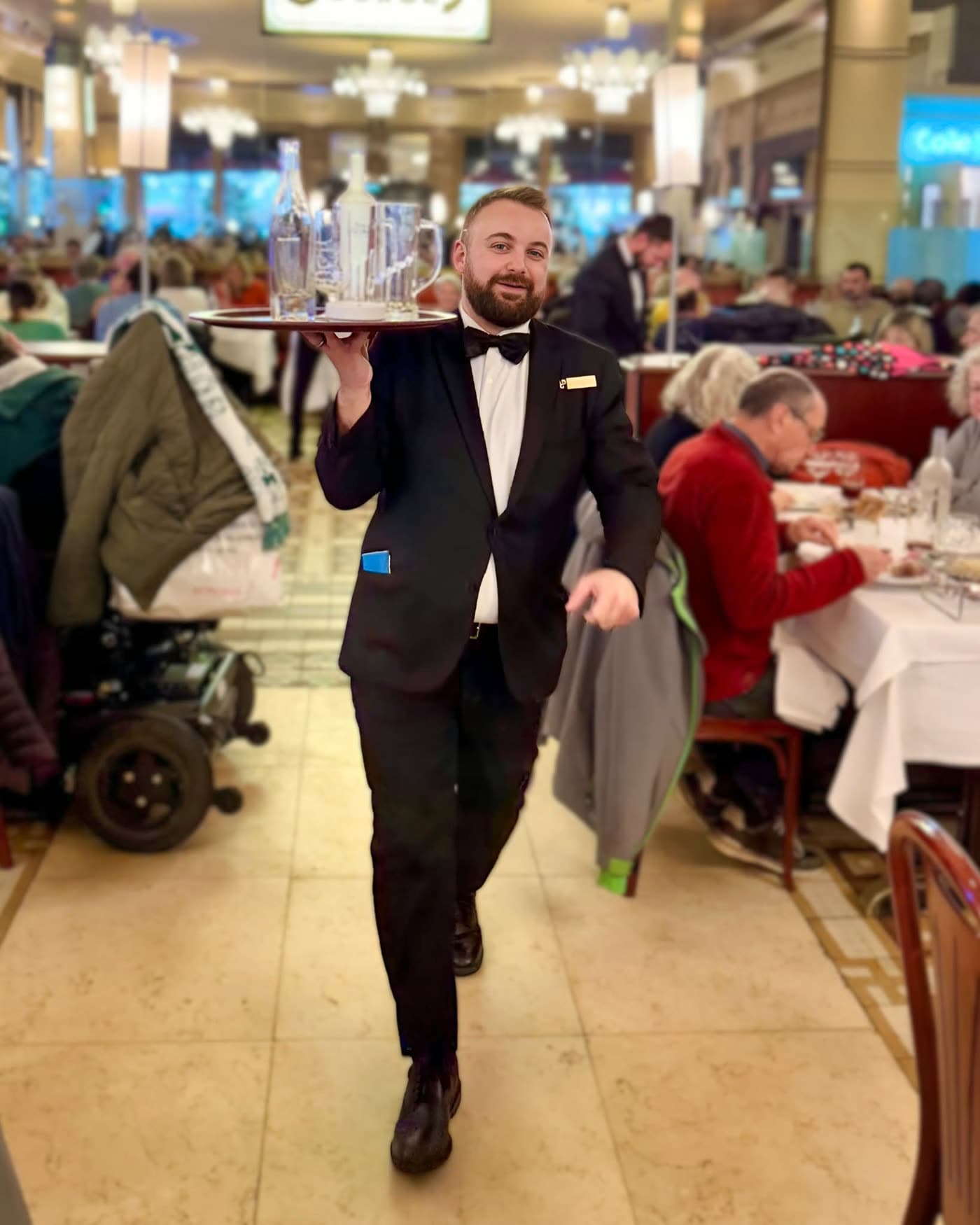 Serveur souriant portant un plateau de verres d'eau en mouvement dans la salle — Brasserie Georges
