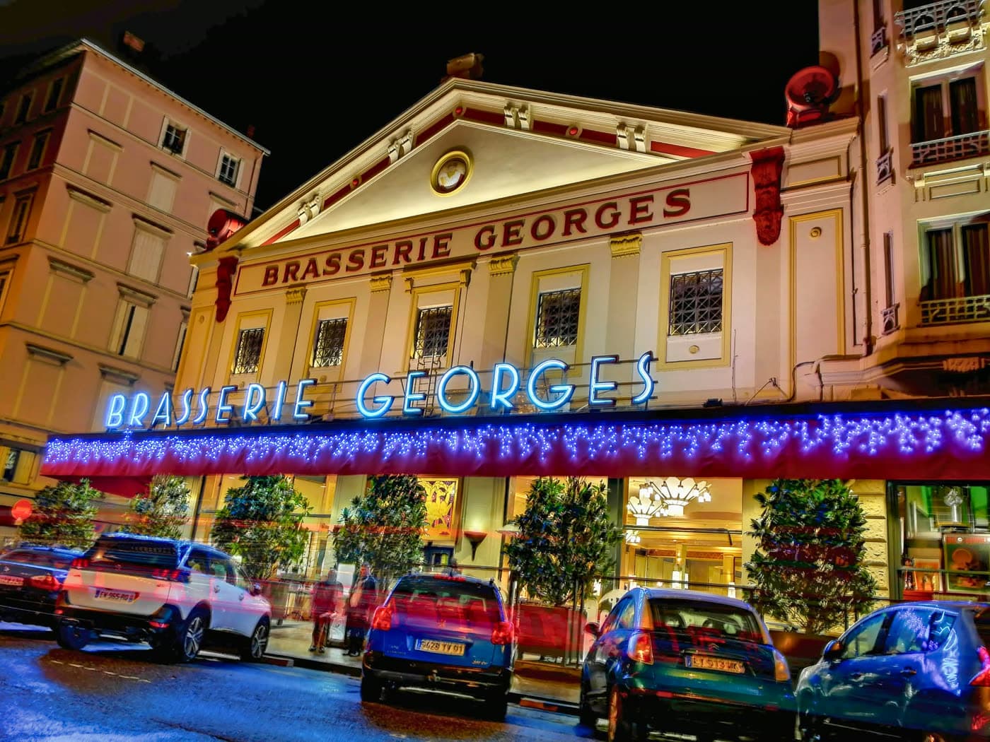 Façade illuminée de nuit avec enseignes lumineuses et guirlandes de fêtes, voitures garées — Brasserie Georges