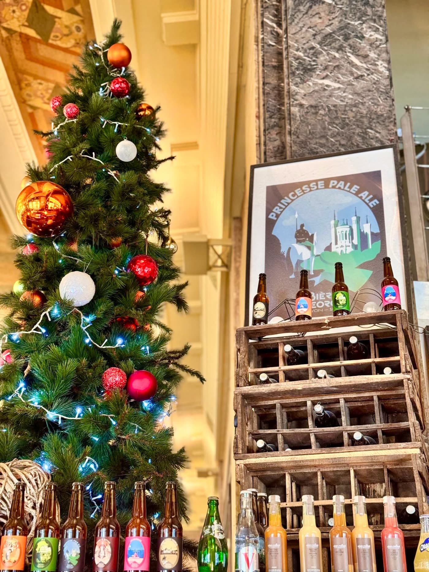 Sapin de Noël à côté d'un présentoir de bouteilles de bières Georges et affiche Princesse Pale Ale — Brasserie Georges