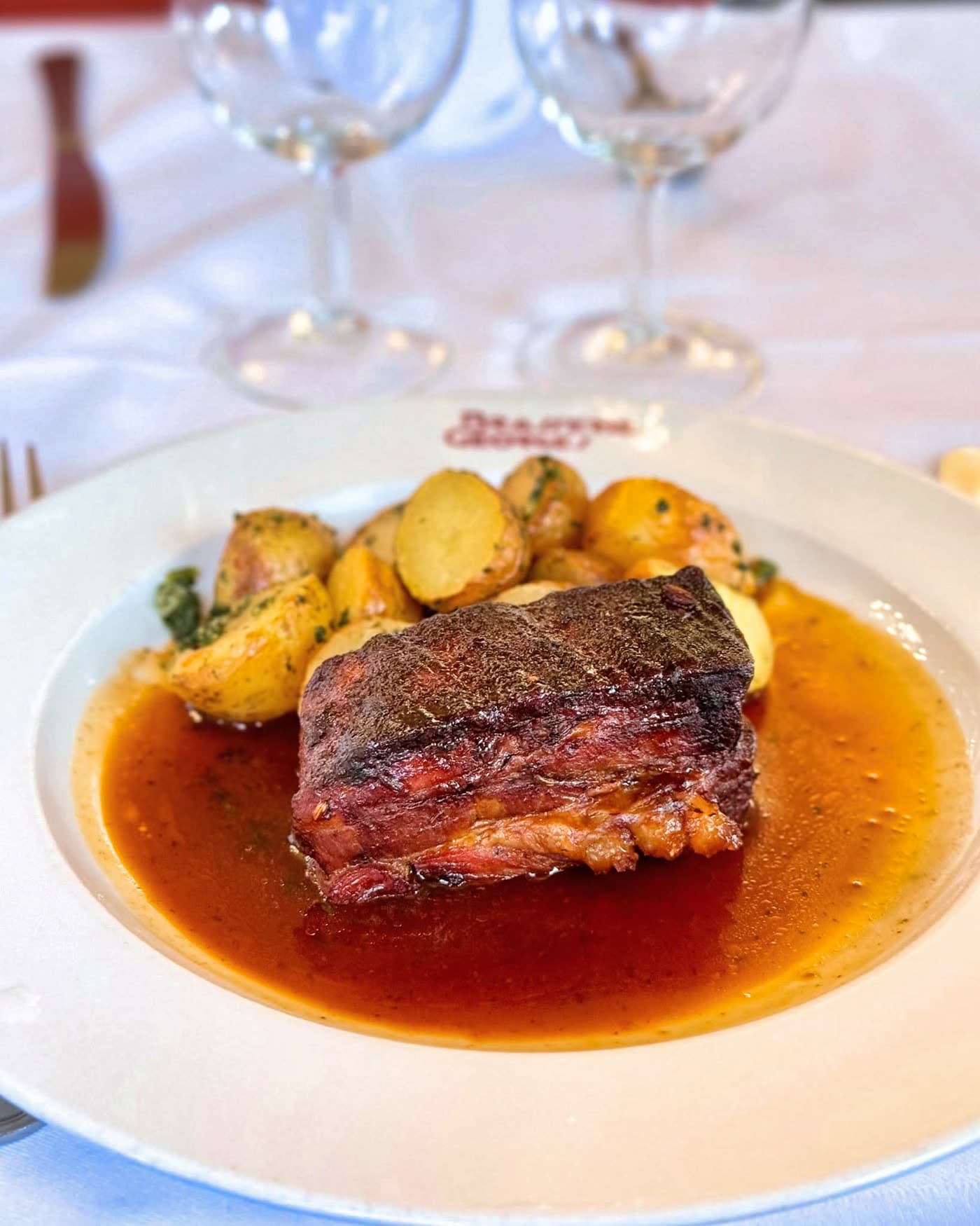 Assiette de viande braisée glacée avec pommes de terre rôties, logo Brasserie Georges visible sur le bord