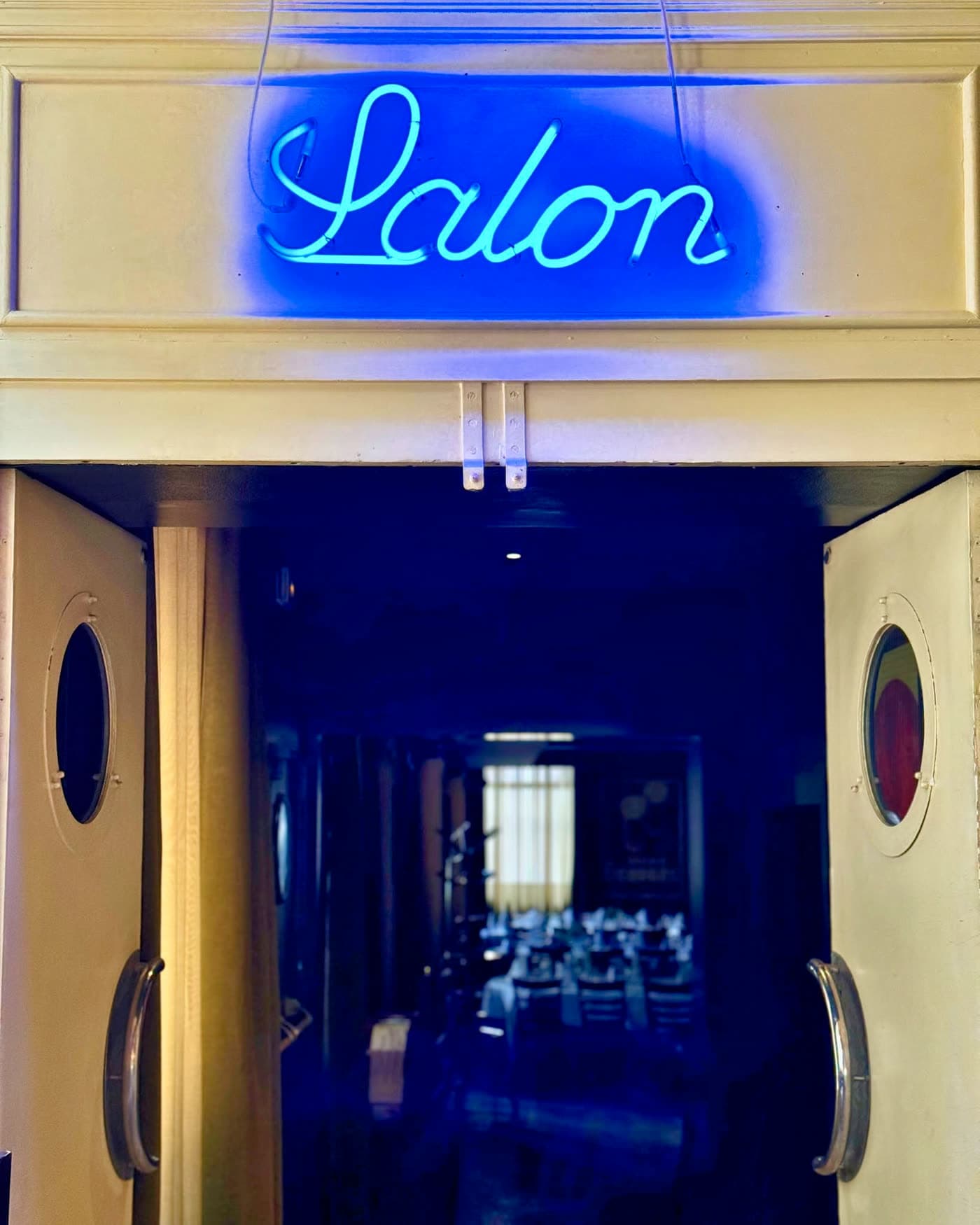 Enseigne néon bleue « Salon » au-dessus de portes battantes ouvertes sur un salon privé sombre — Brasserie Georges