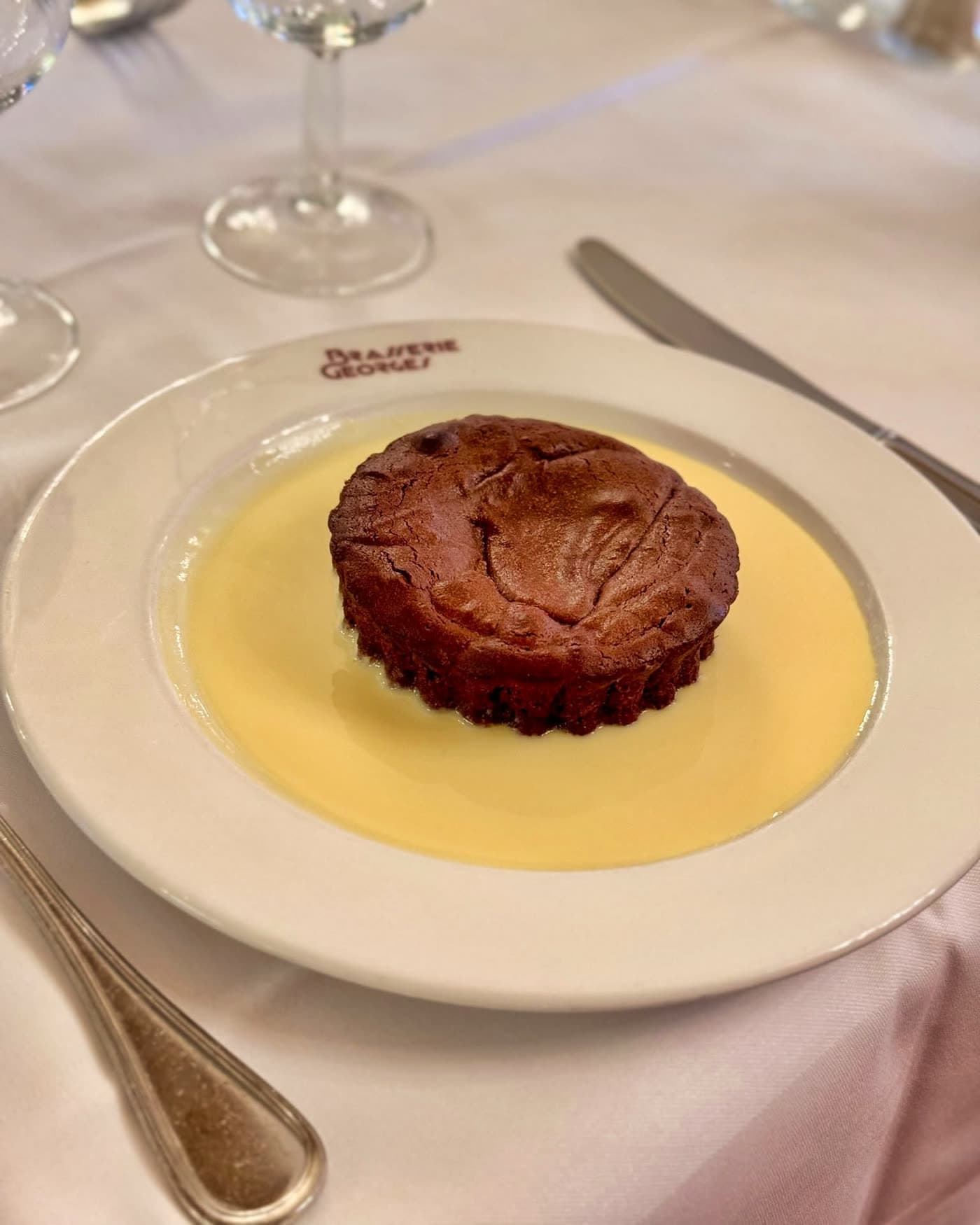 Fondant moelleux rond nappé de crème anglaise sur assiette Brasserie Georges, cuillère en accompagnement