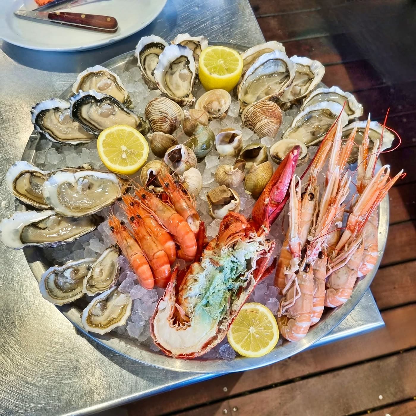 Plateau de fruits de mer avec huîtres, palourdes, langoustines et demi-langouste sur glace, table en bois extérieure — Brasserie Georges