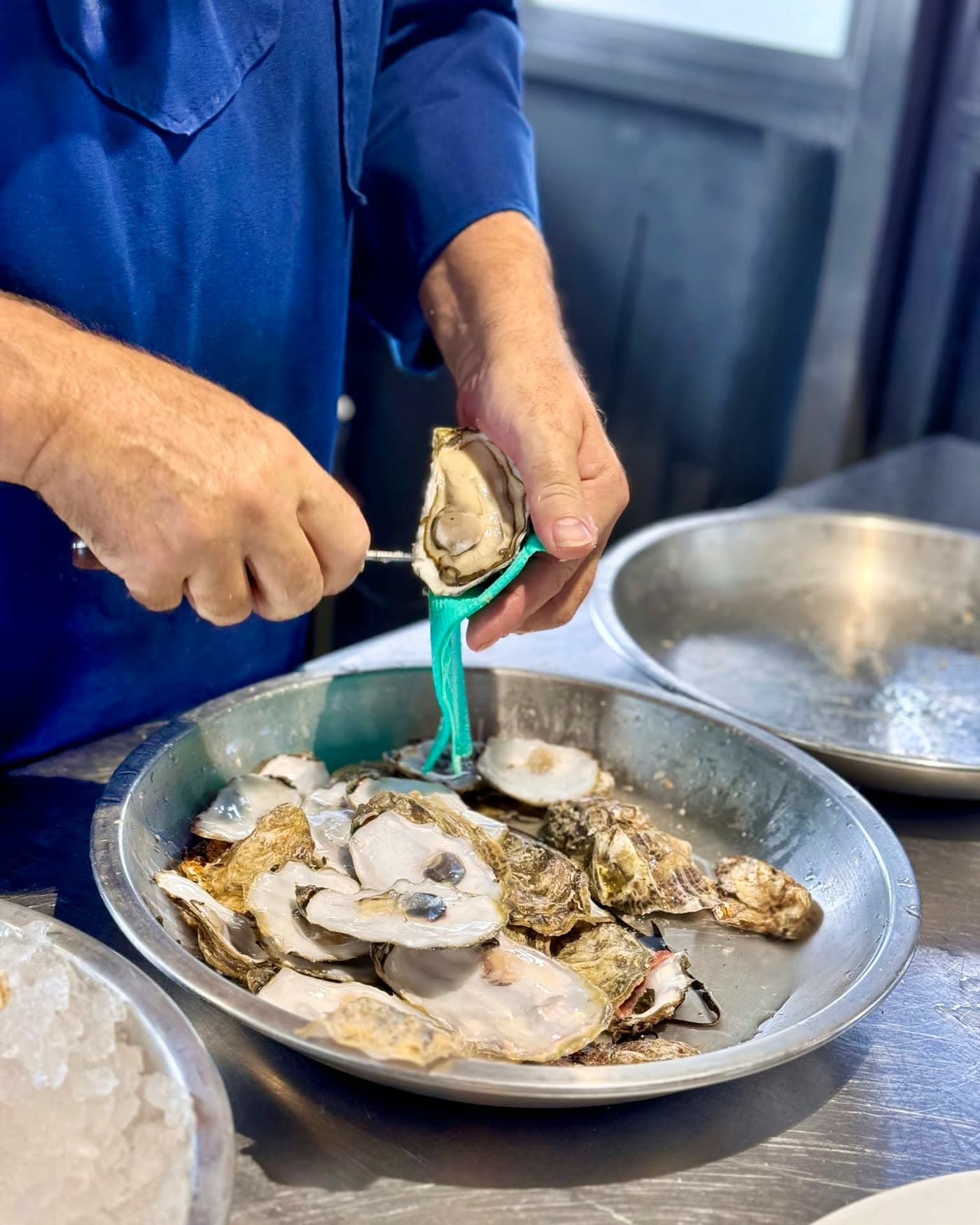 Gros plan sur des mains ouvrant une huître au couteau au-dessus d'un plateau métallique — Brasserie Georges