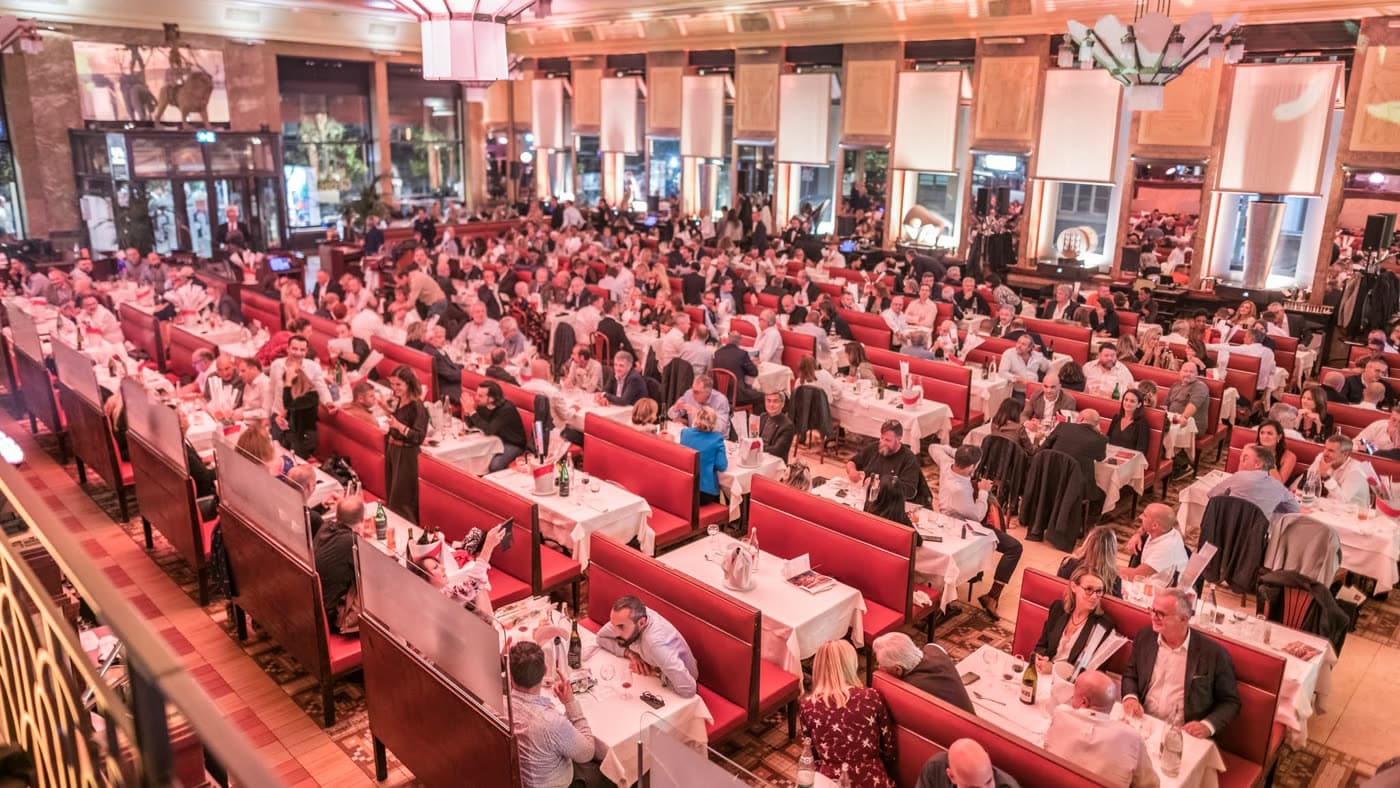 Vue en hauteur de la salle entière avec banquettes rouges, sol à motifs géométriques et clients dispersés — Brasserie Georges