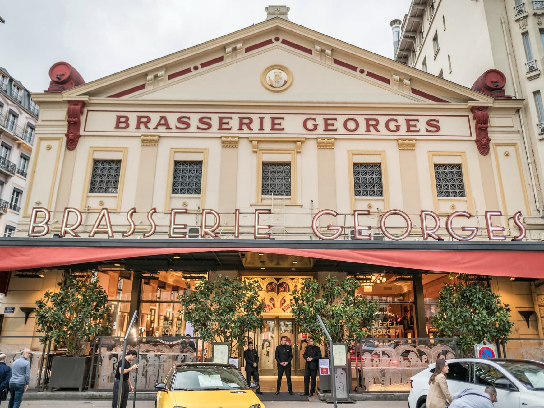 Façade de la Brasserie Georges de jour avec fronton, enseigne rouge et auvent, entrée avec personnel