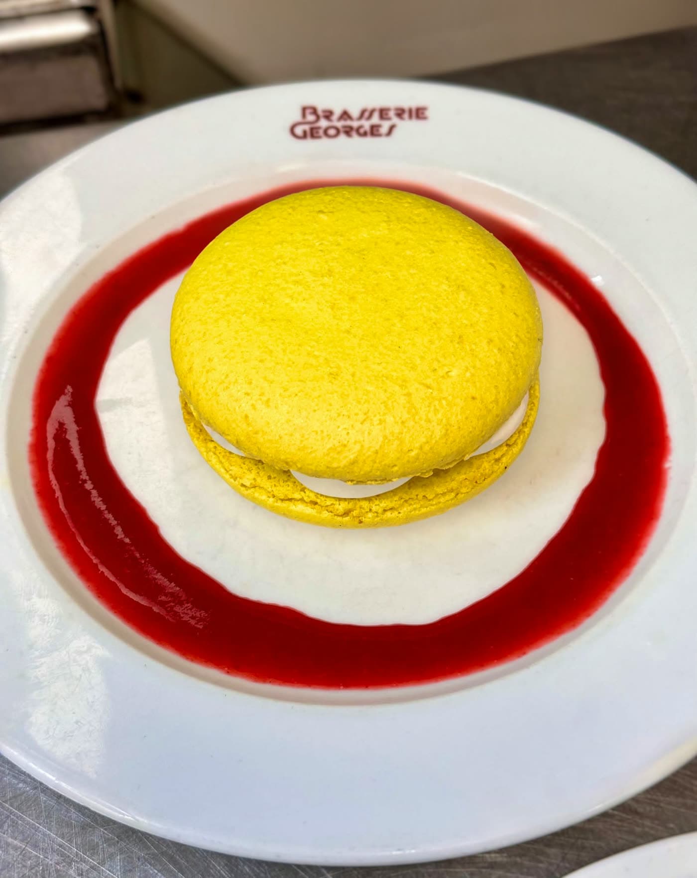 Macaron géant jaune sur assiette Brasserie Georges, coulis de fruits rouges en cercle