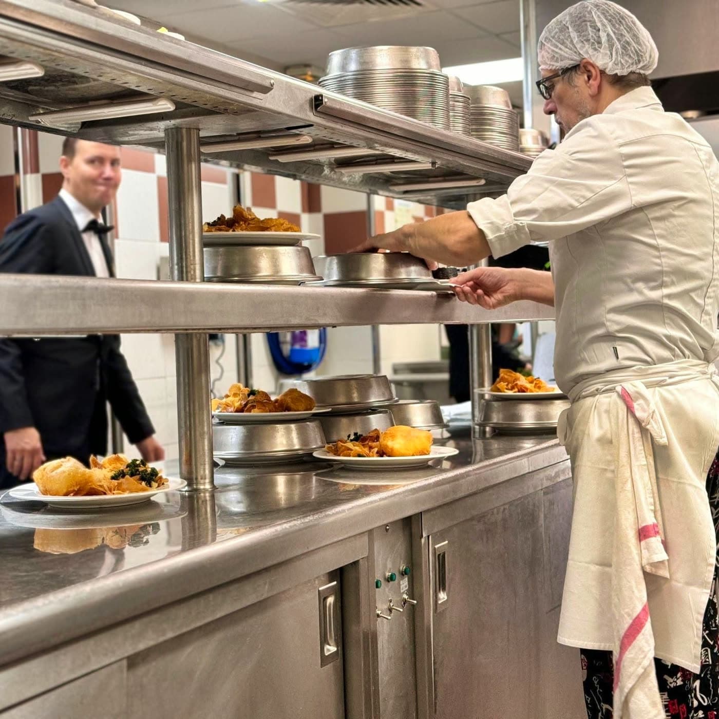 Chef dresse des assiettes au passe pendant qu'un serveur attend en cuisine — Brasserie Georges