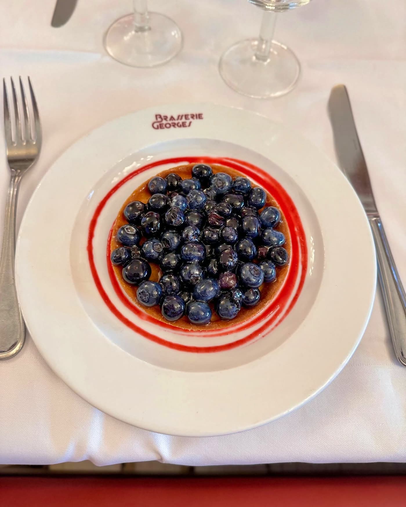 Tarte aux myrtilles nappée d'un trait de sauce rouge, dressée sur table avec verres à vin — Brasserie Georges