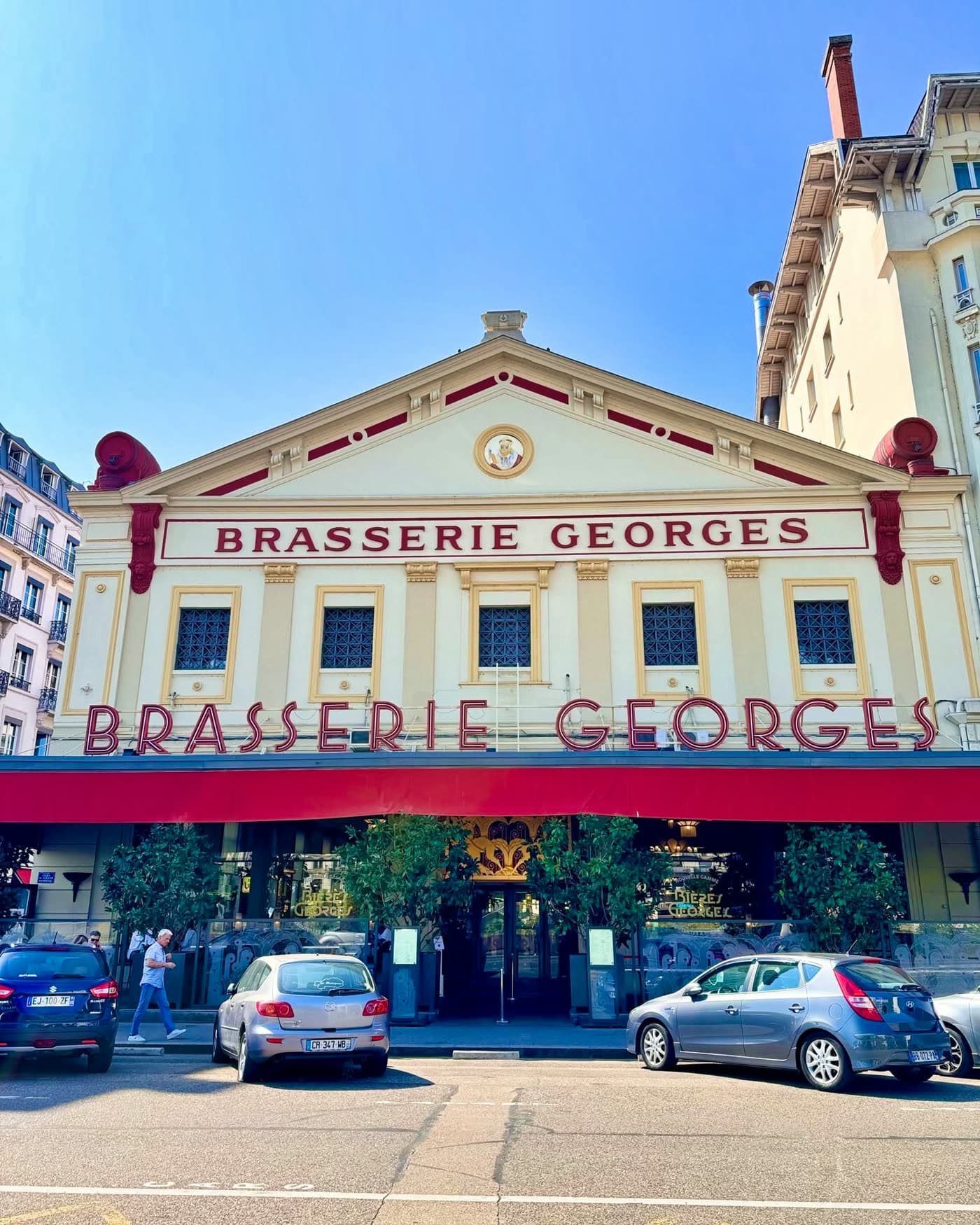 Façade Brasserie Georges de jour, ciel bleu, voitures garées devant