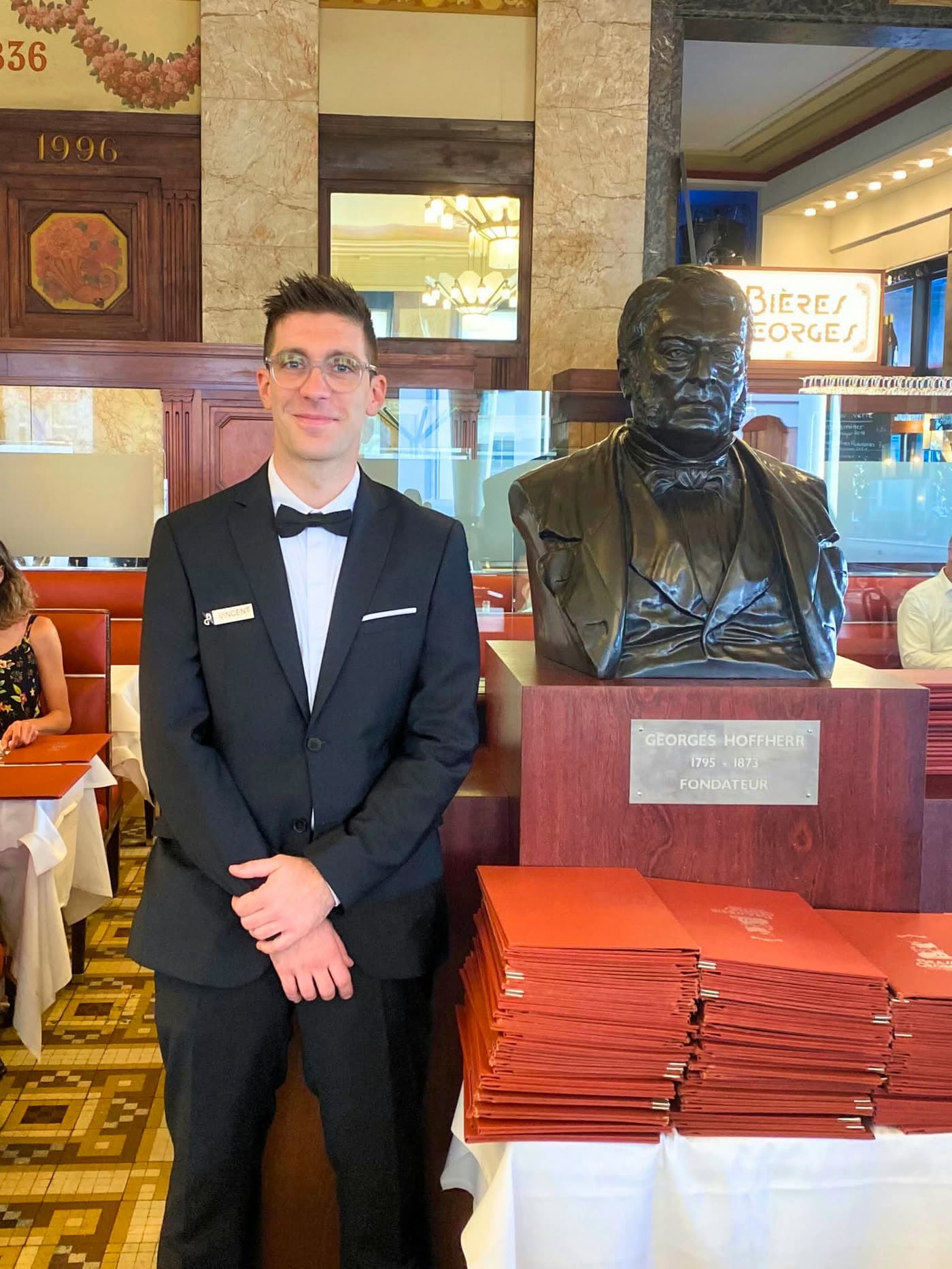 Serveur en costume posant près du buste du fondateur Georges Hofherr — Brasserie Georges