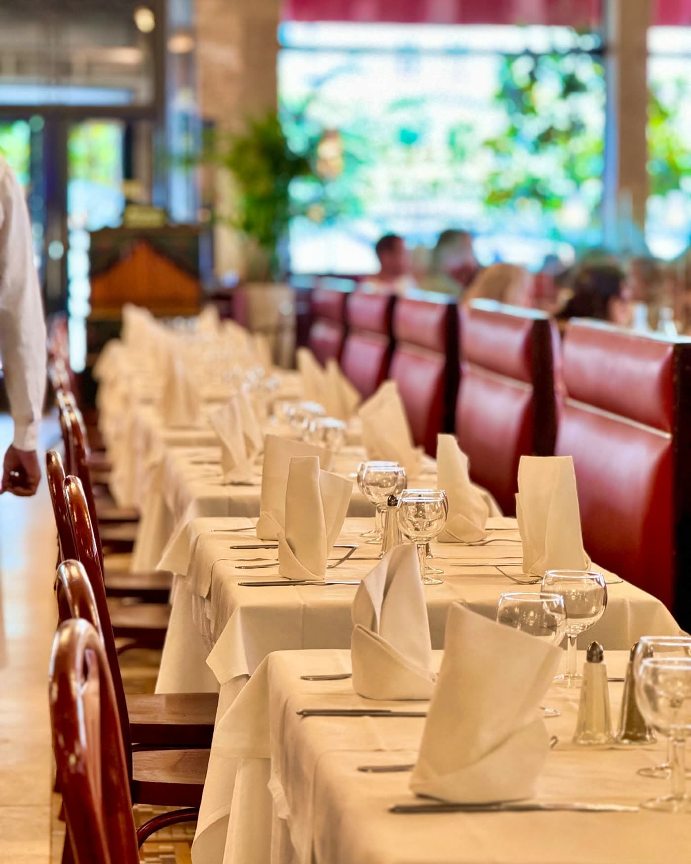 Longue rangée de tables dressées avec banquettes bordeaux, vue en enfilade — Brasserie Georges