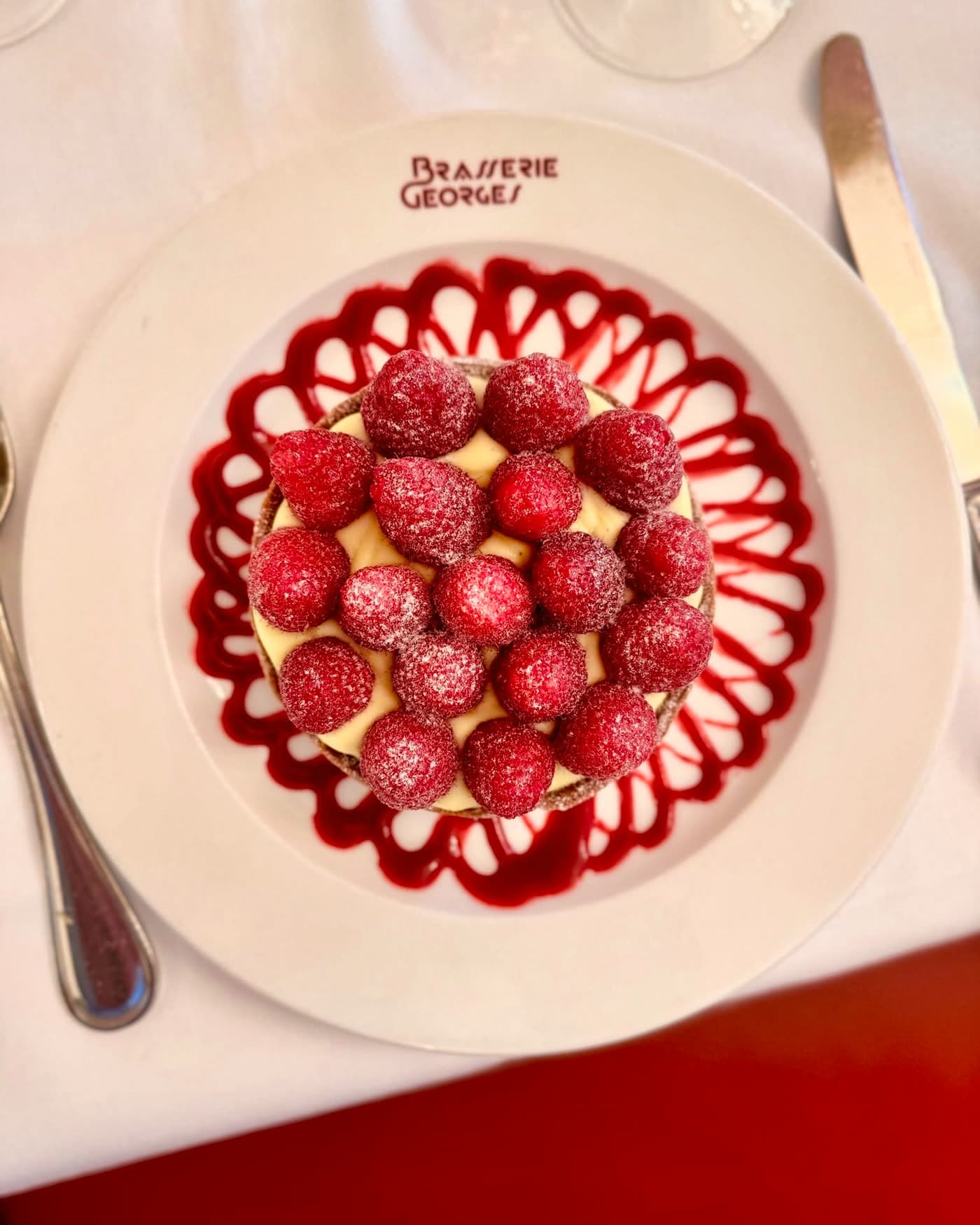 Tarte aux fruits sur assiette siglée, banquettes rouges floues en fond — Brasserie Georges