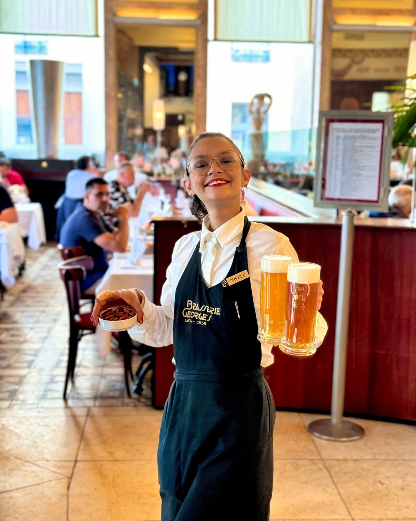 Serveuse souriante tenant deux chopes de bière et une coupelle — Brasserie Georges
